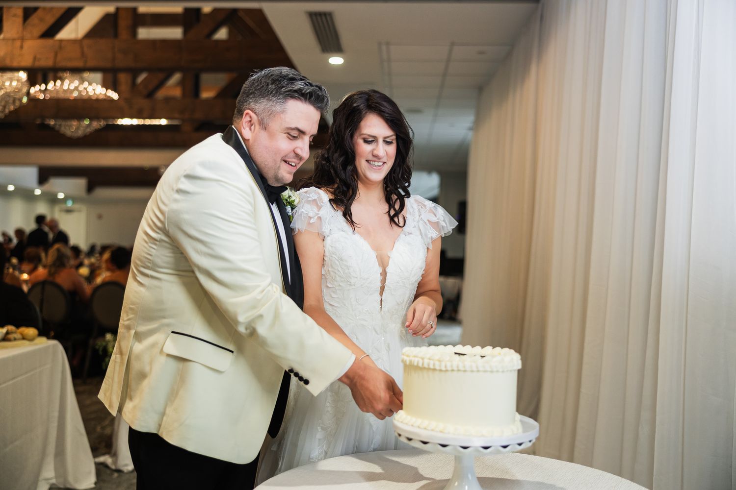 Bride and groom cutting their white wedding cake together at an elegant indoor wedding reception.