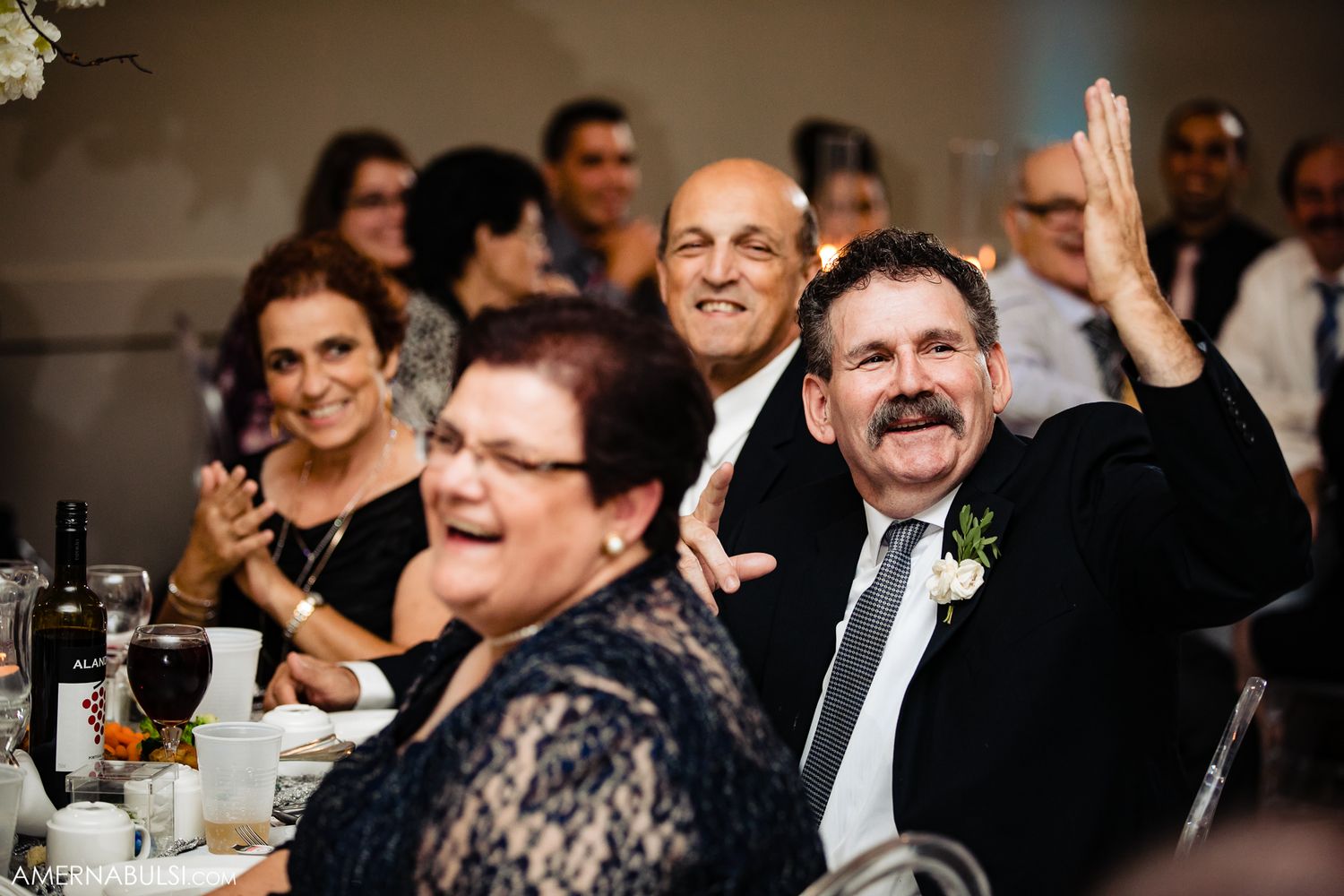 Wedding guests share laughter and joy during an elegant reception dinner in a dimly lit banquet hall.
