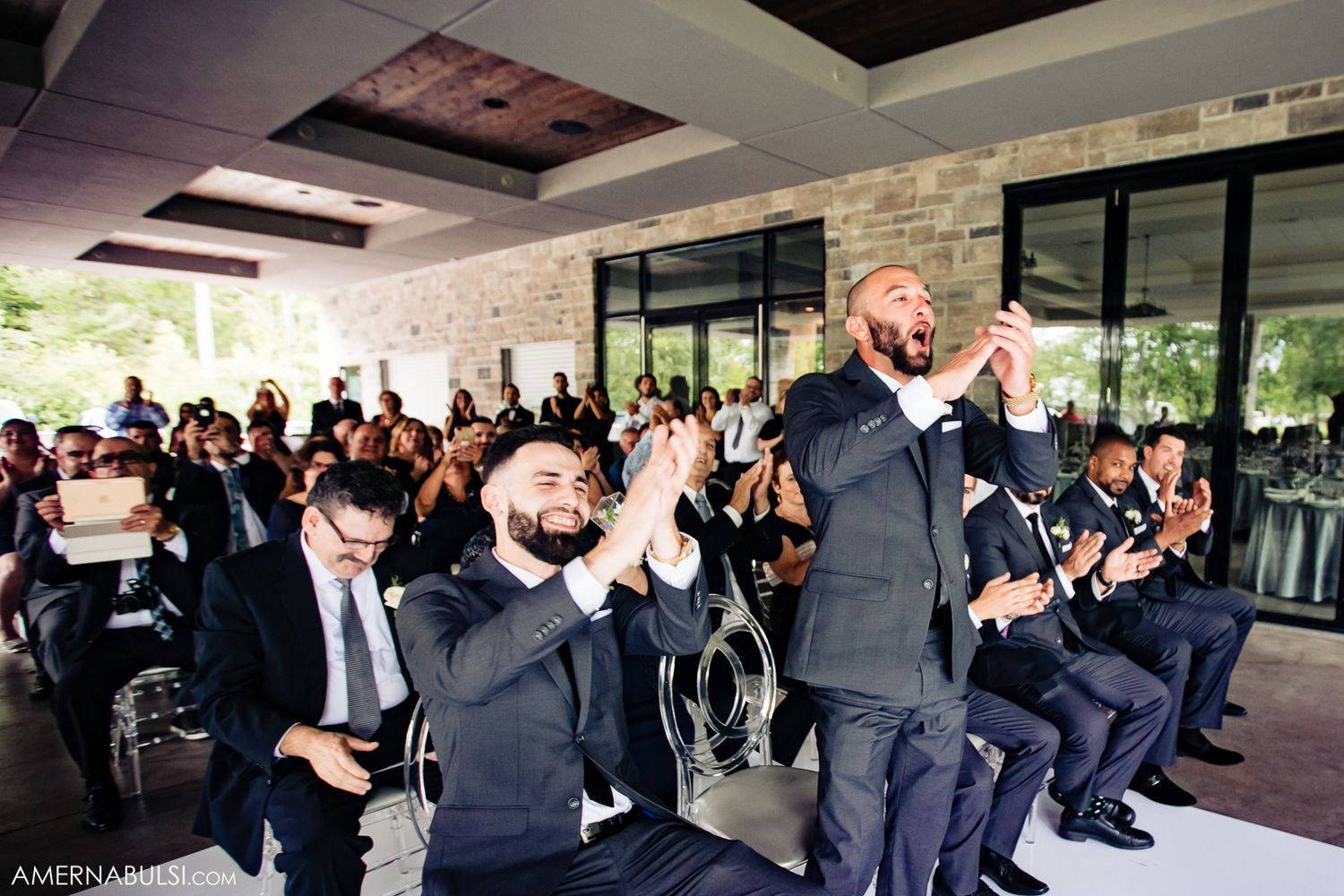 Groomsmen in dark suits sitting and cheering during wedding celebration.