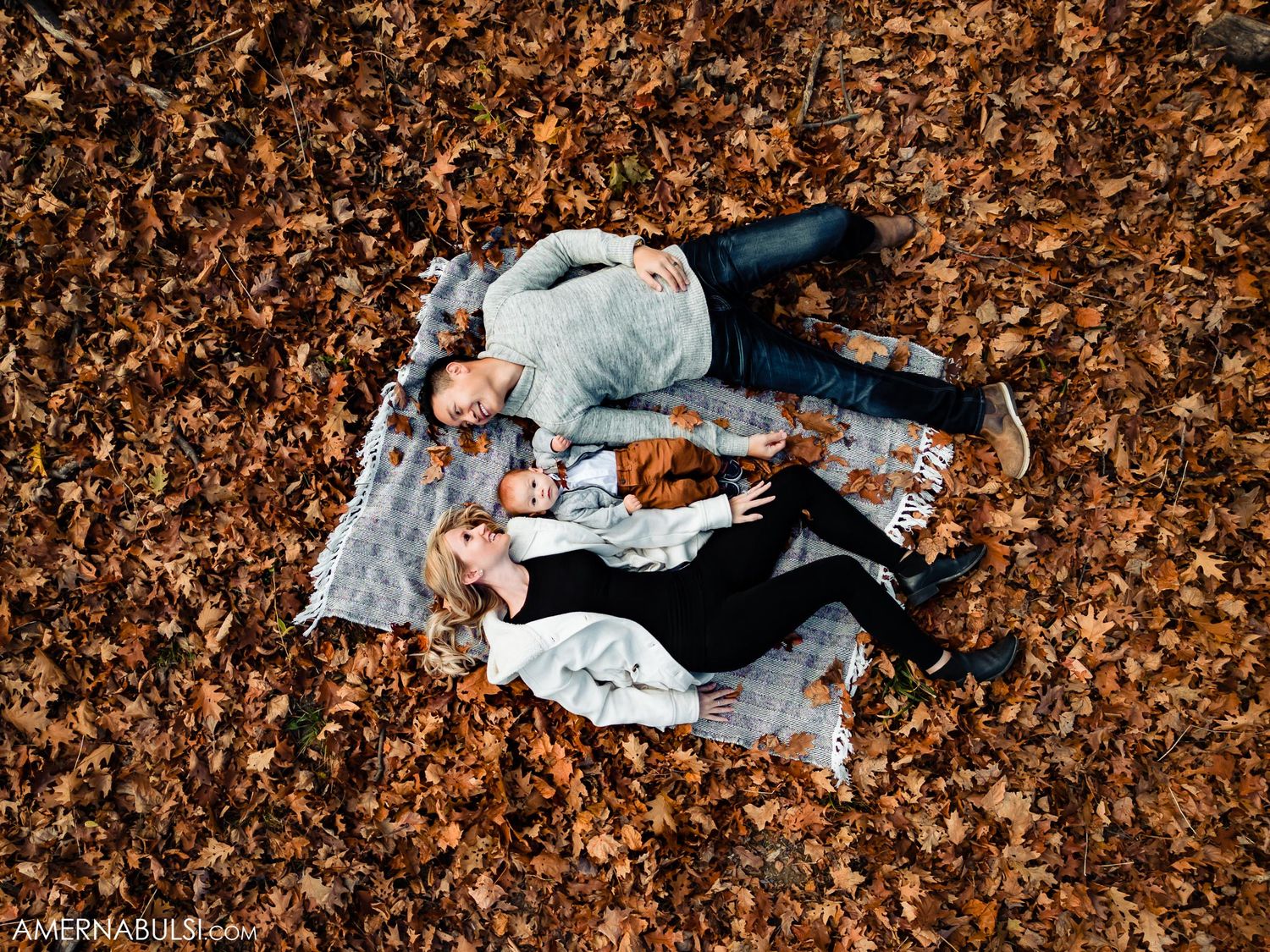 Aerial view of couple lying on blanket surrounded by autumn leaves in a park setting.