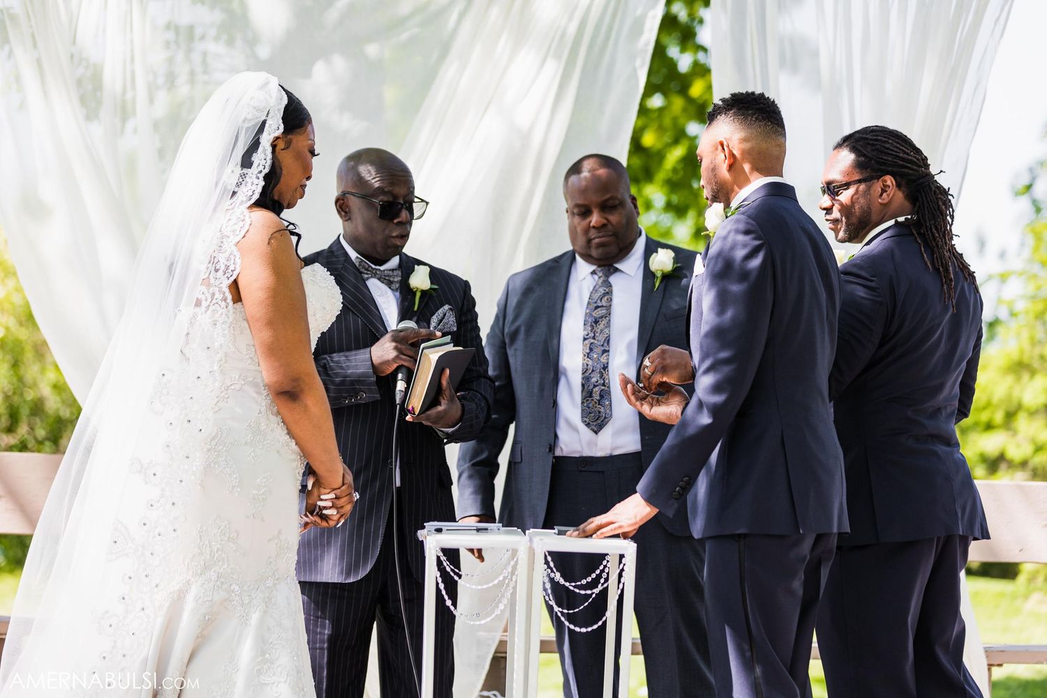 Outdoor wedding ceremony under white fabric draping with wedding party gathered around altar.