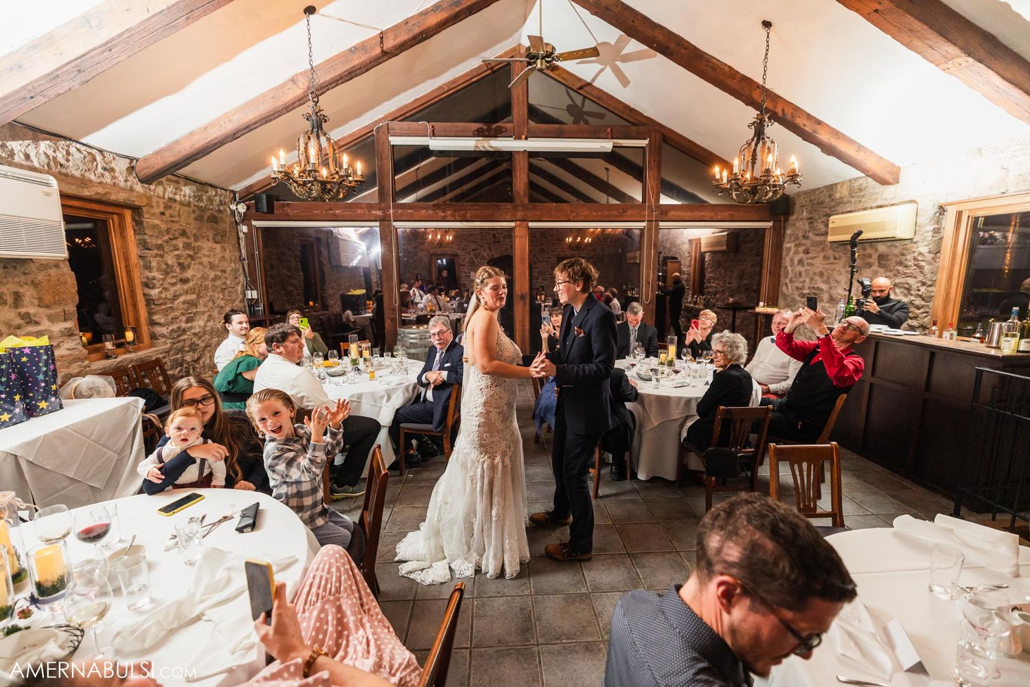 Wedding celebration in a rustic stone venue with exposed wooden beams and elegant table settings.