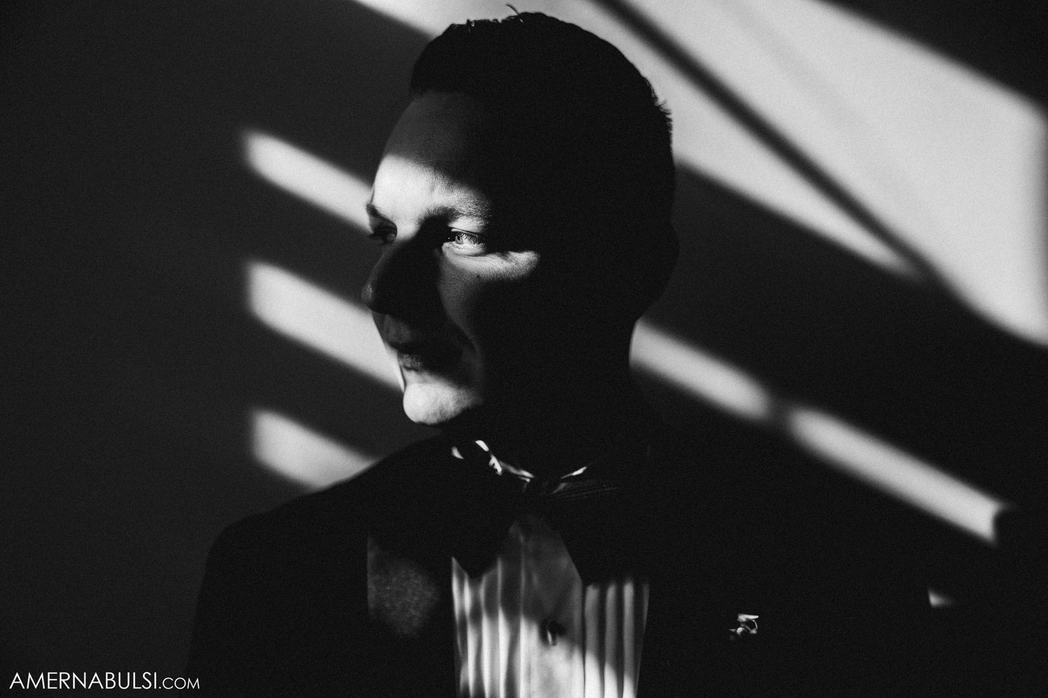 Artistic black and white portrait with venetian blind shadows creating dramatic lighting.