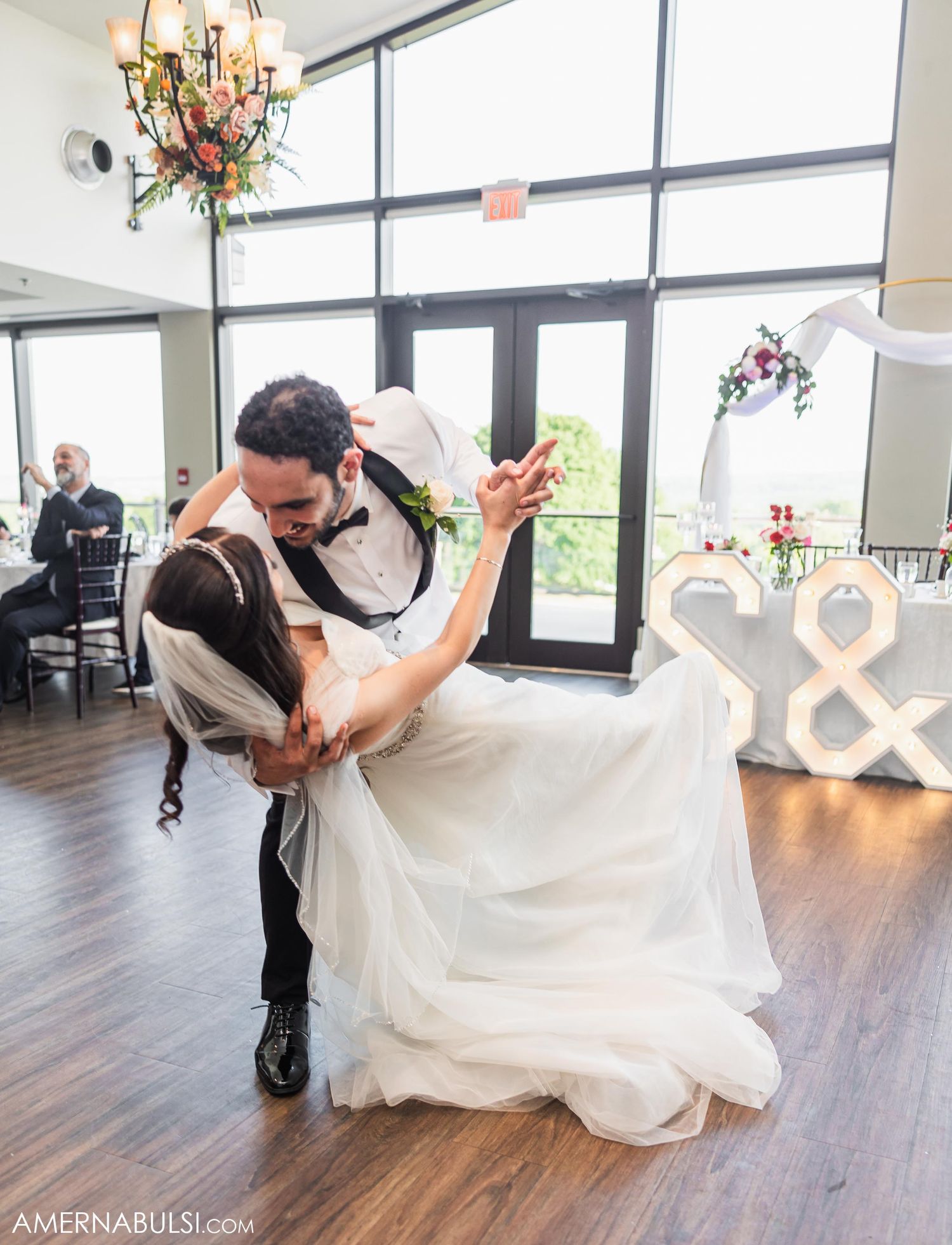 Romantic dip dance between newlyweds on wooden dance floor with decorative lighting.