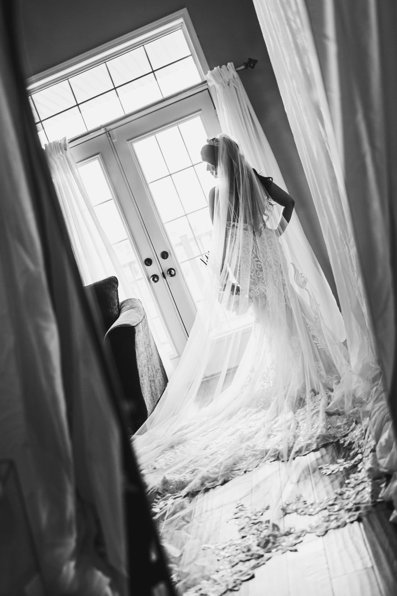 Black and white photo of a flowing wedding dress veil silhouetted against French doors.