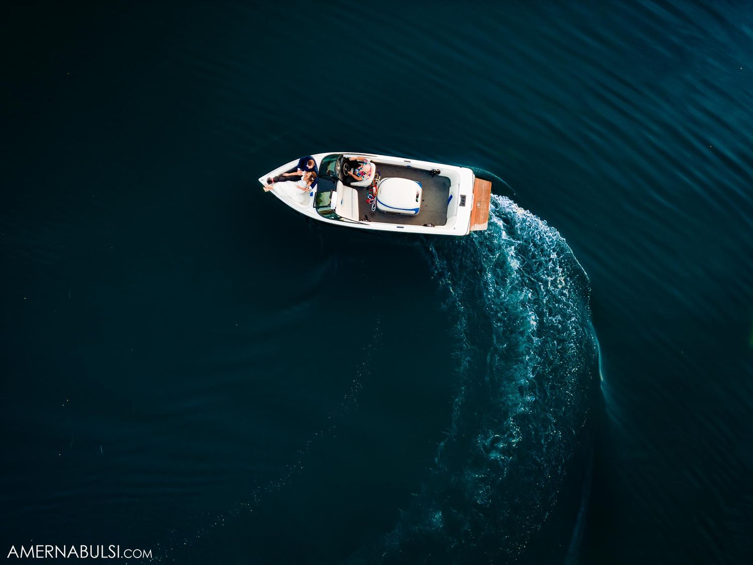 Drone shot of a white speedboat creating a wake in dark blue water.