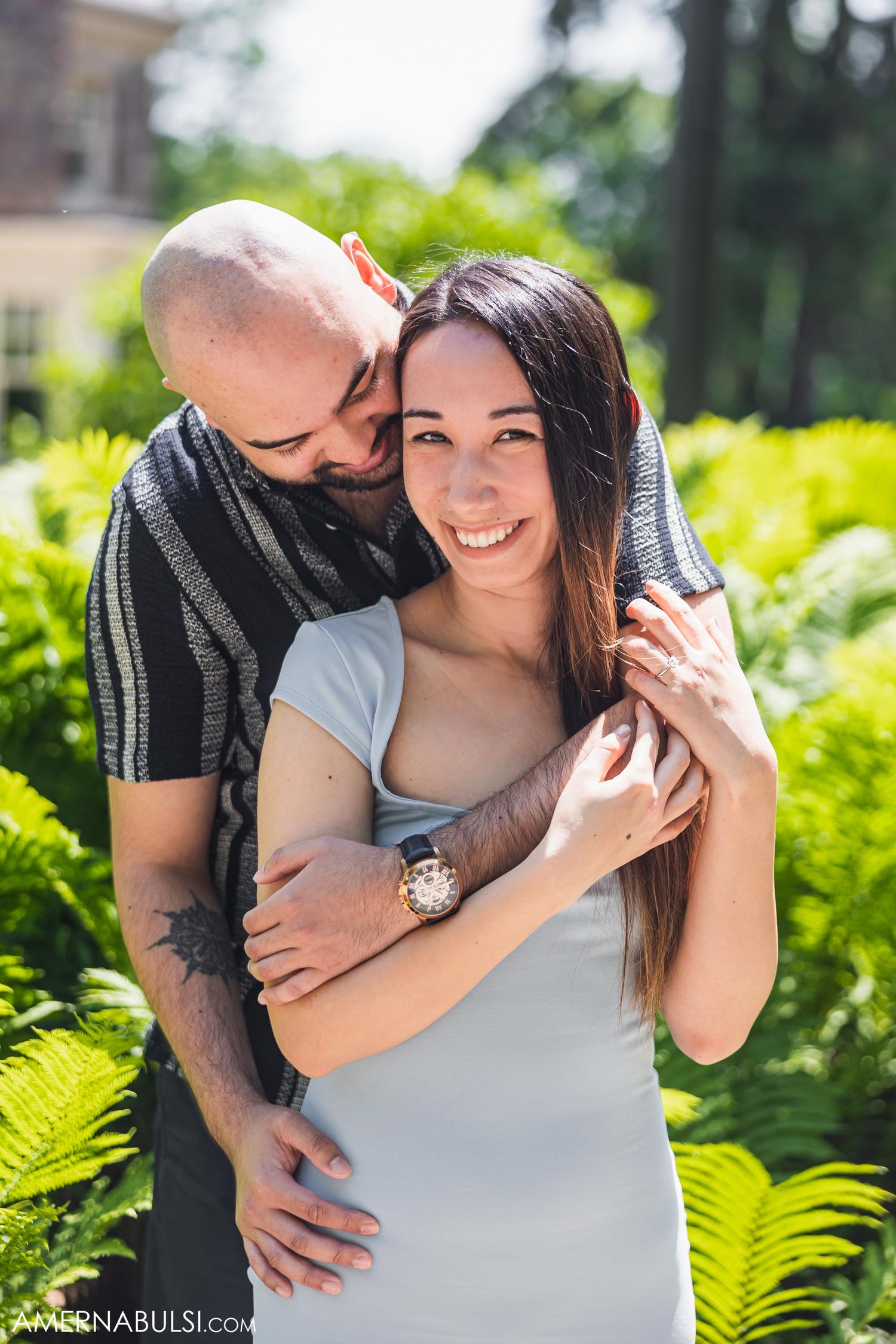 A romantic couple embraces in a lush garden with ferns on a sunny day.