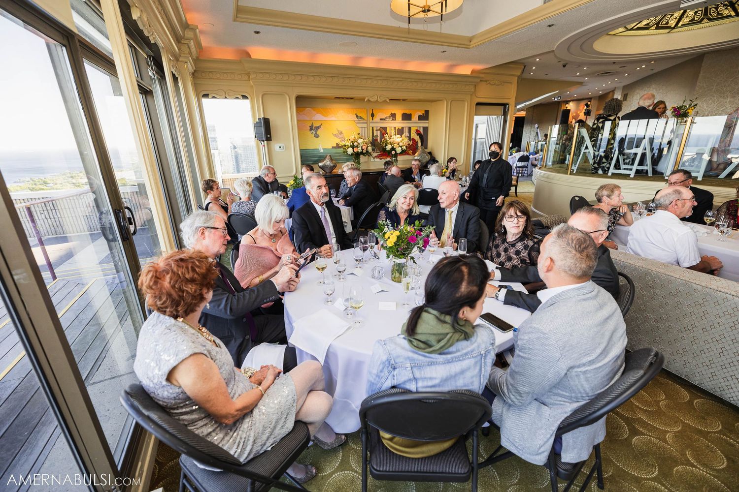 Large dining room filled with guests seated at round tables during an elegant event.