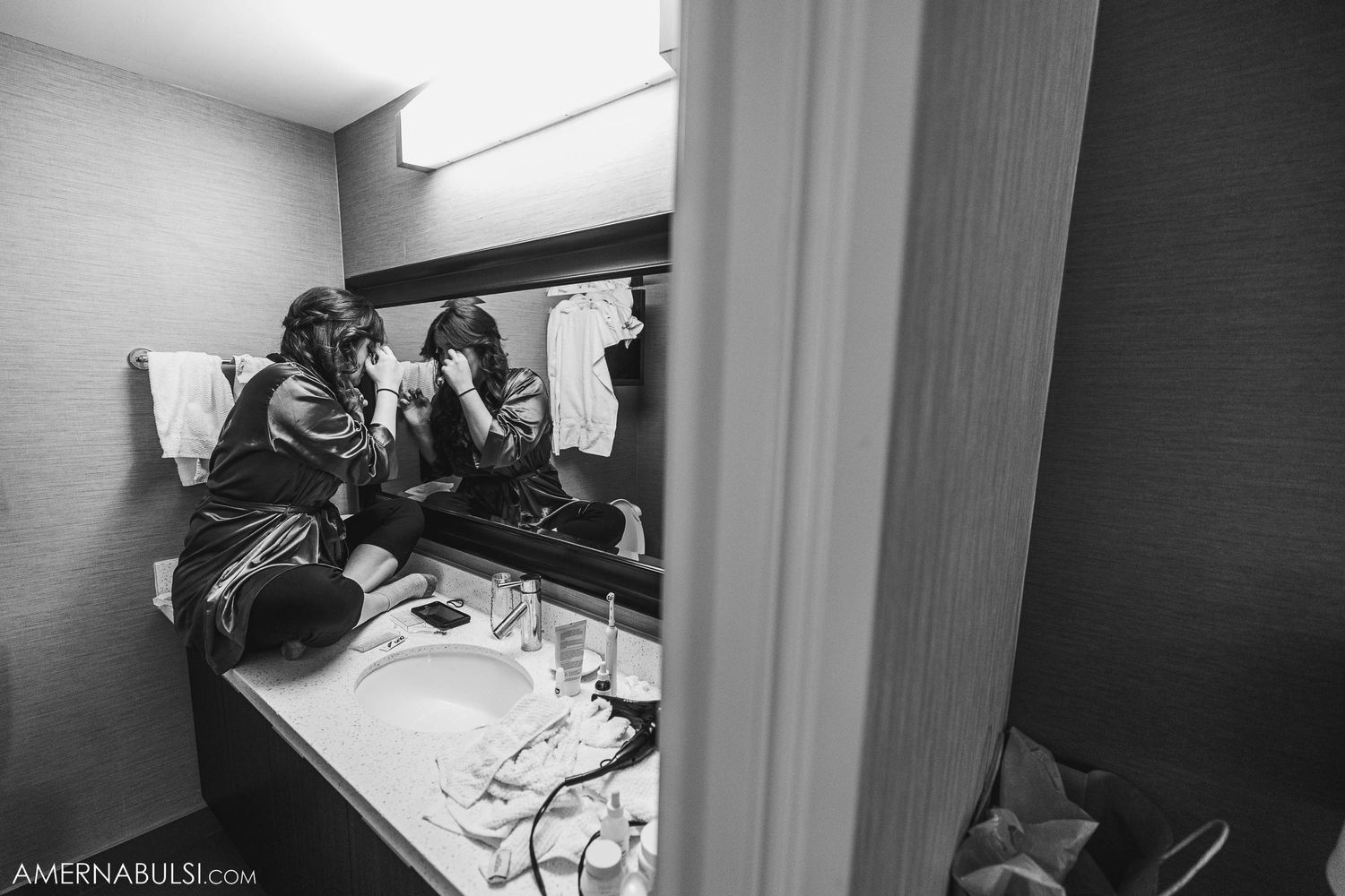 Black and white image of people getting ready at a bathroom vanity counter.