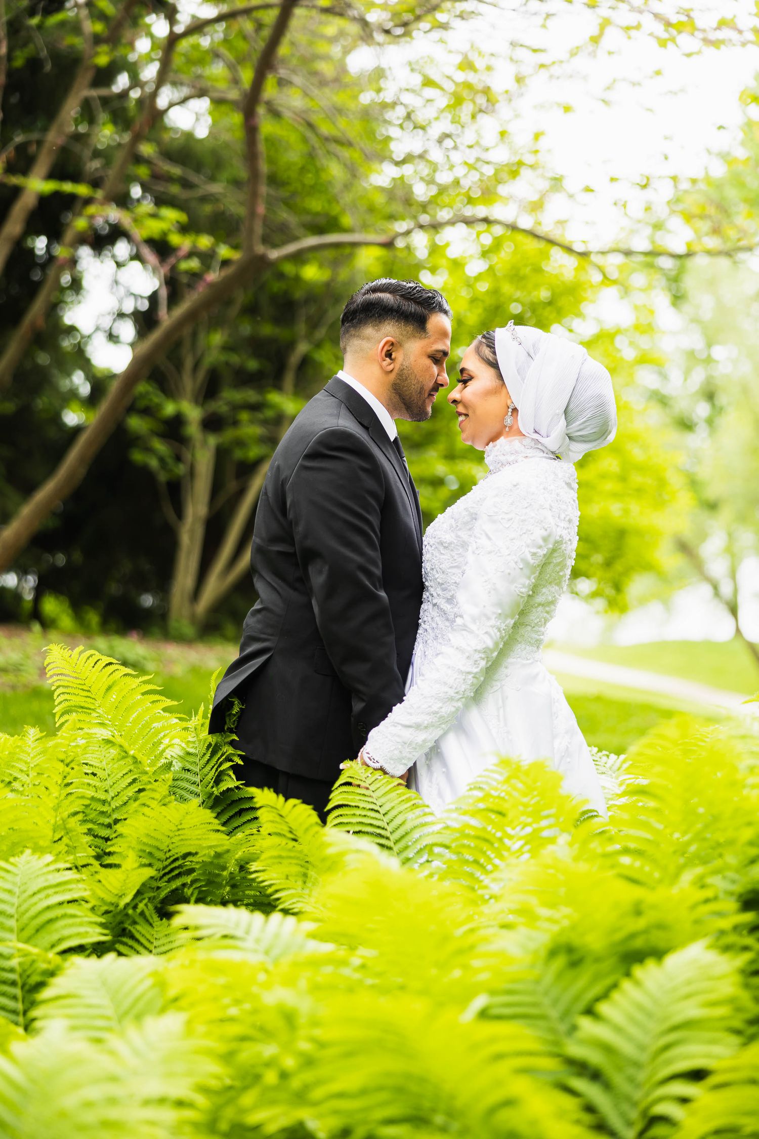 Newlyweds share an intimate moment among green ferns in a garden setting.