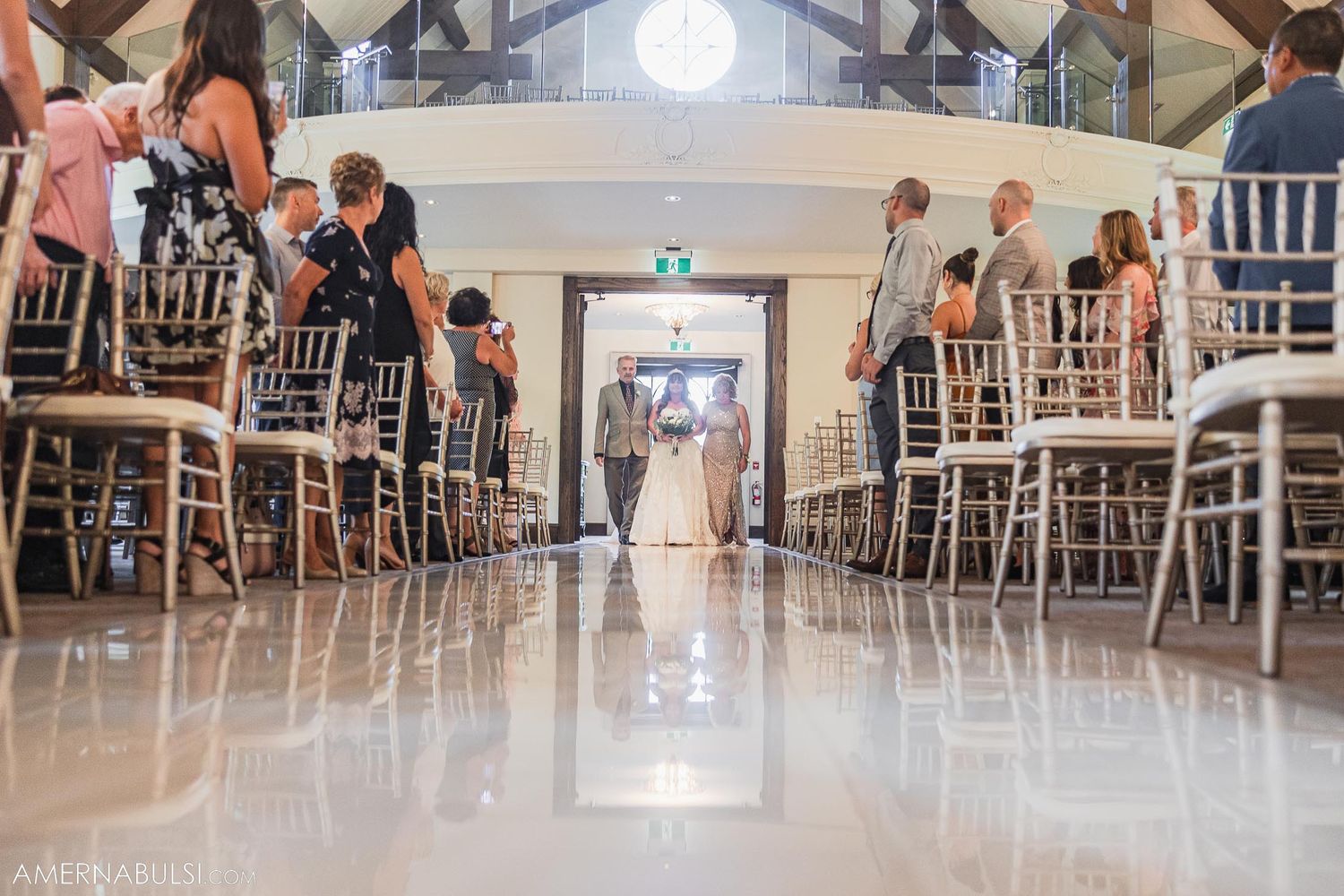 View down aisle with white chairs and wooden beams overhead in elegant wedding chapel.