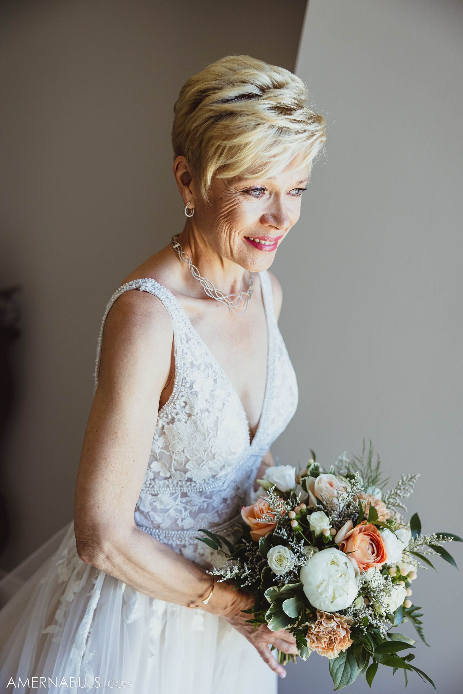 Bride in lace wedding dress holds elegant bouquet of peach and white flowers.