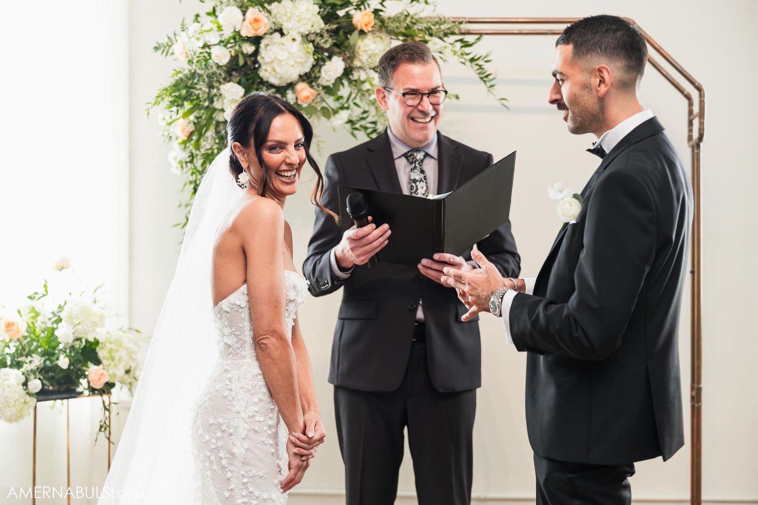 Wedding ceremony in progress with couple and officiant under floral decorated arch.