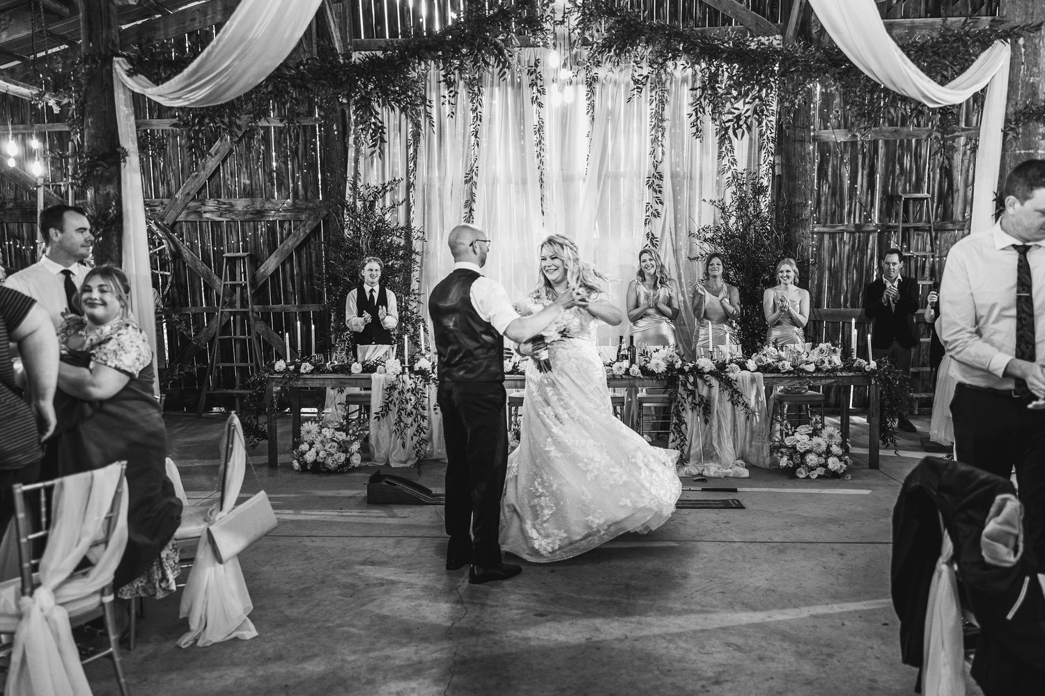 Black and white photo of wedding ceremony in rustic venue with elegant draping and decorations.