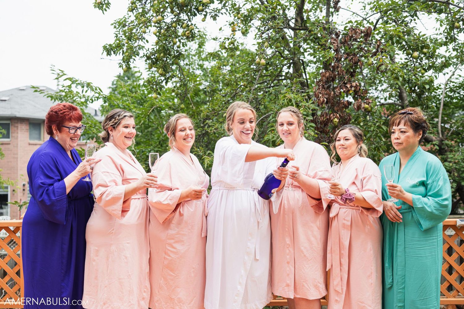 Group wearing pink and colored robes standing together outdoors for a pre-wedding photo.