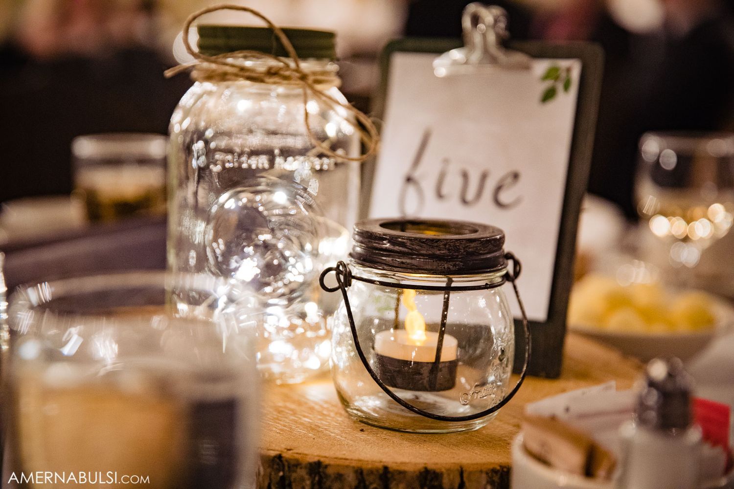 Rustic wooden tables set with glowing lanterns and candles for an intimate wedding reception.