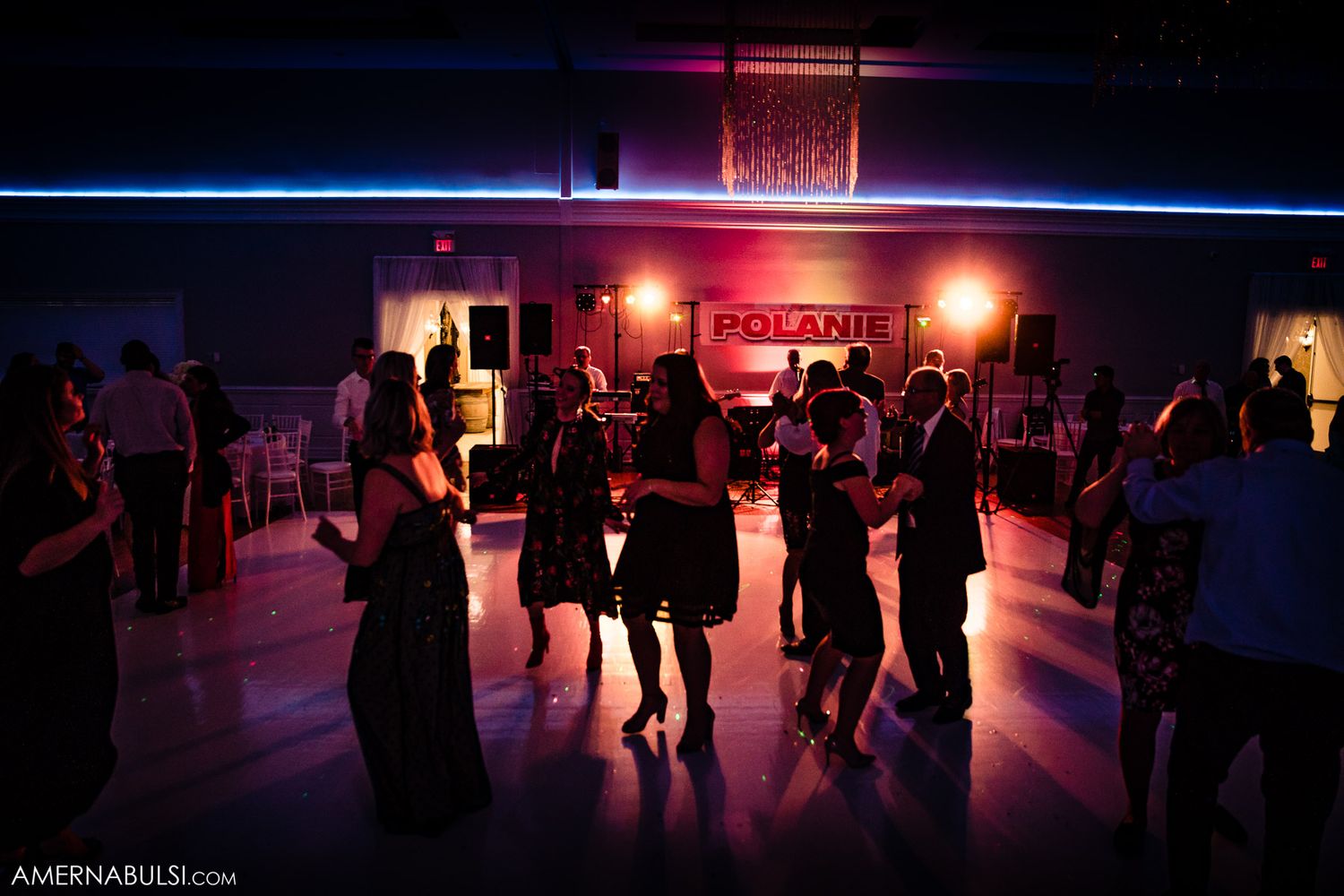 Silhouettes of people dancing in a dimly lit ballroom with colorful lighting creating a romantic atmosphere.