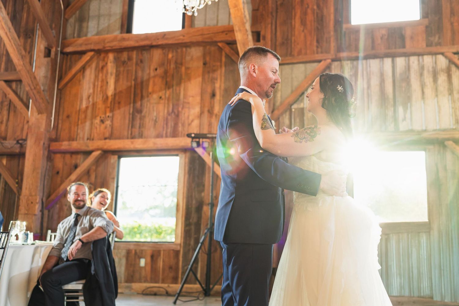 Newlyweds share their first dance in a sunlit rustic barn venue.