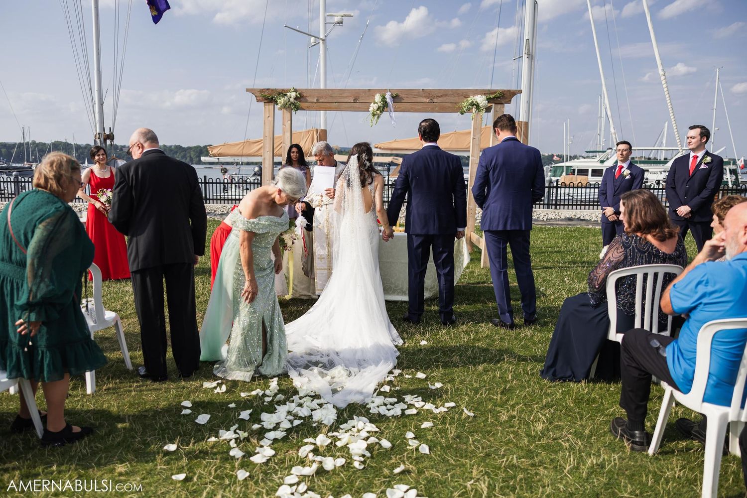 A wedding ceremony setup on grass with white chairs and marina views in the background.