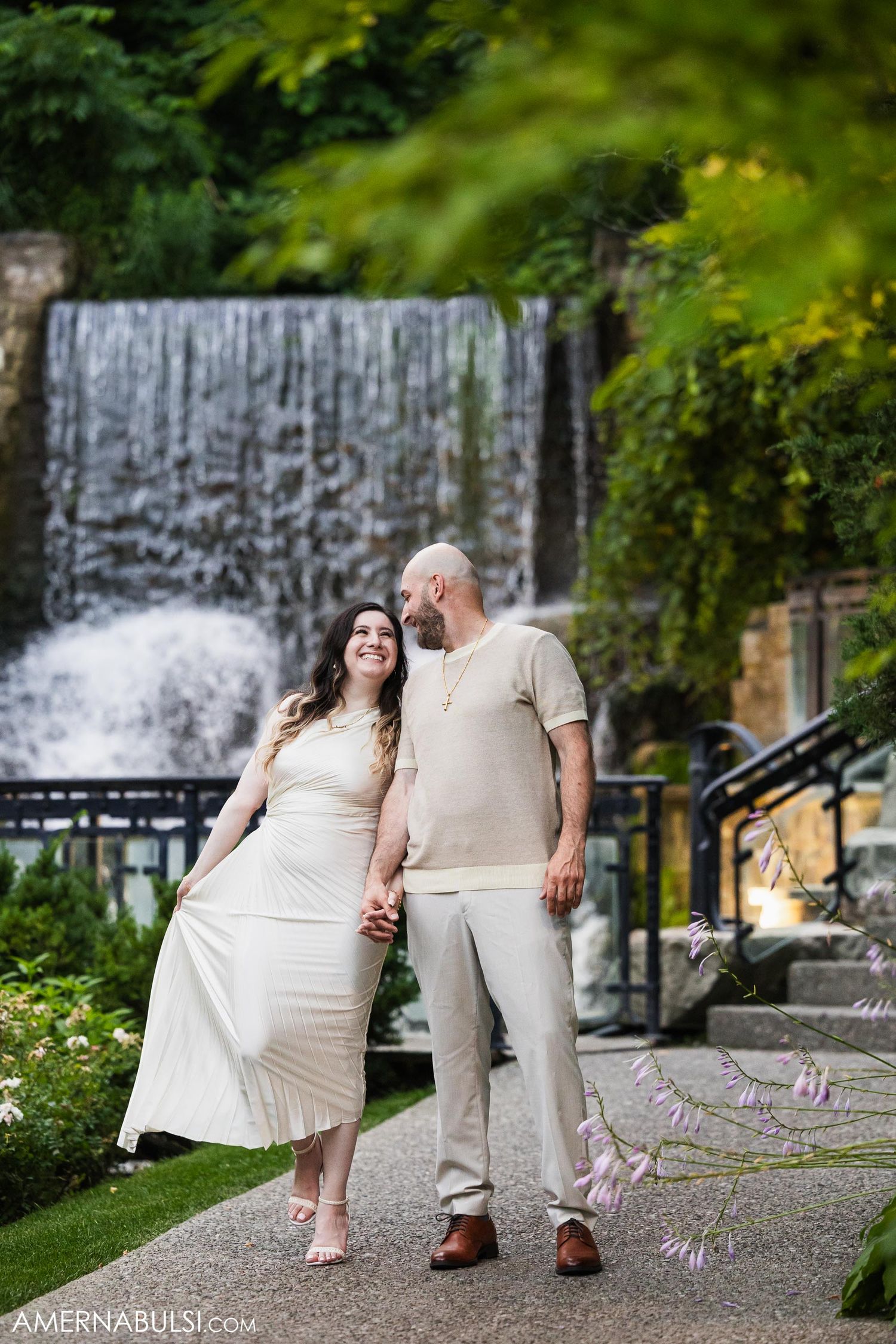 Couple in light-colored outfits sharing a tender moment by a cascading waterfall.