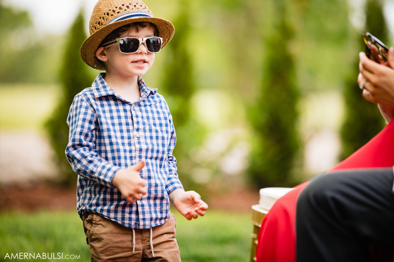 A child in a plaid shirt and straw hat plays outdoors during a sunny summer day.
