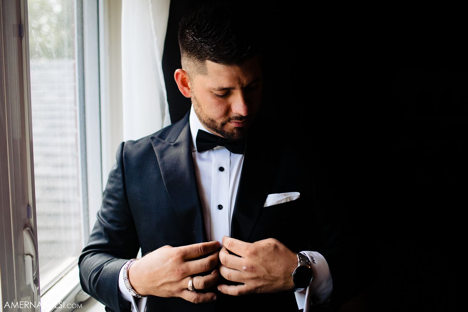 Close-up shot of a groom adjusting his bowtie in formal attire.
