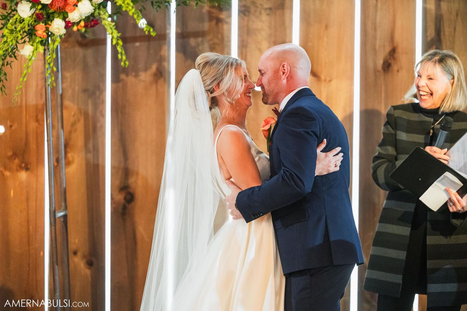 Wedding ceremony taking place in rustic barn venue with wooden walls and floral decorations.