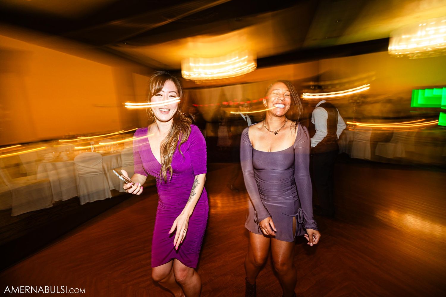 Two wedding guests dance energetically on a dimly lit dance floor with motion blur effects.