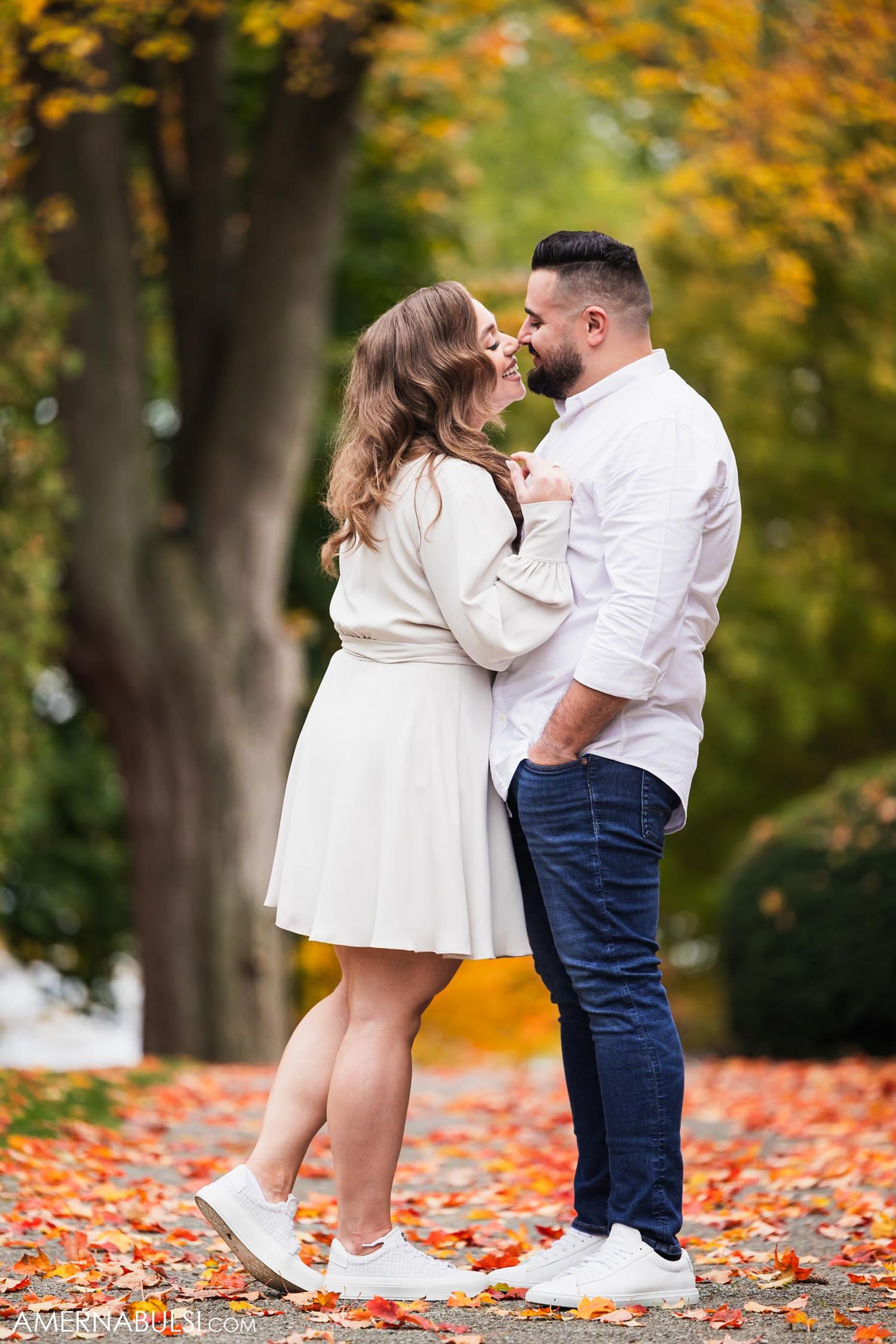 A romantic autumn engagement photo with fallen leaves covering the ground.