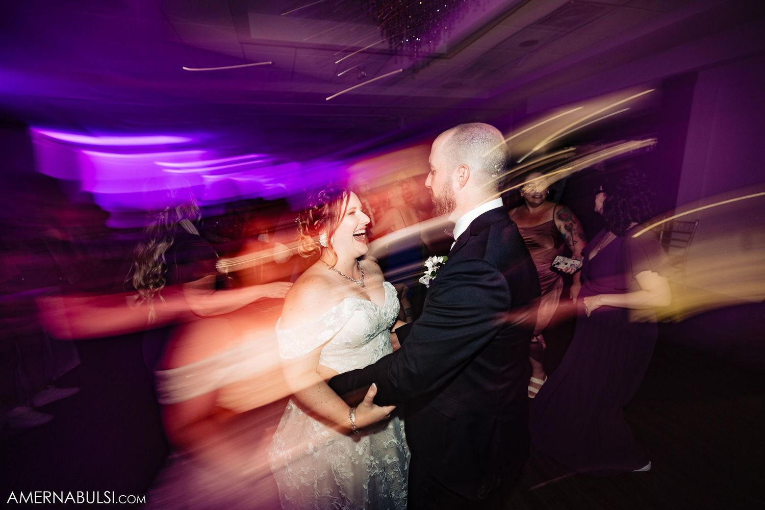 Motion blur capture of dancing at wedding reception with purple lighting effects.
