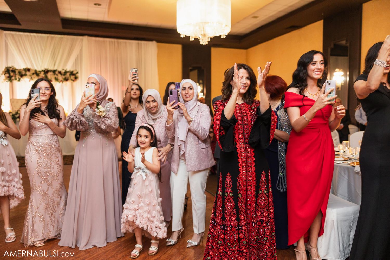 Wedding guests in formal attire applauding and celebrating during reception festivities.