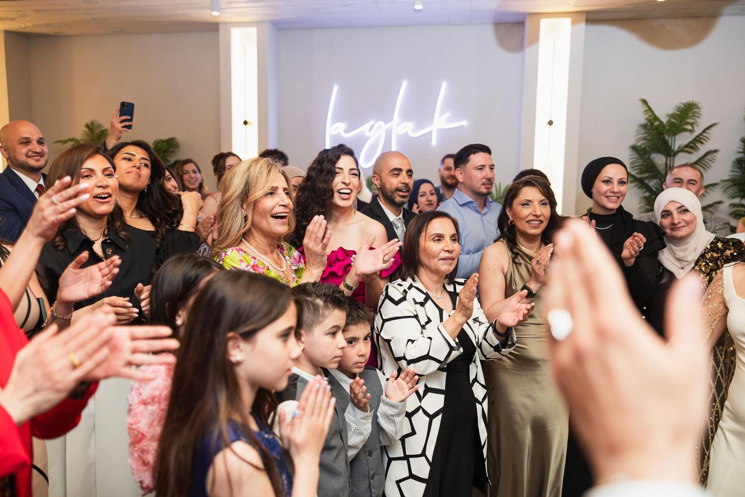 Excited wedding guests cheering with a neon sign glowing in the background.