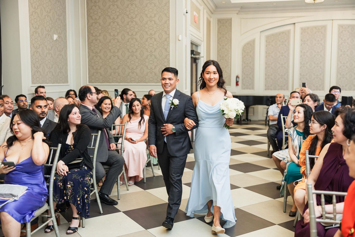 Wedding party proceeds down elegant checkered aisle with guests seated on either side.
