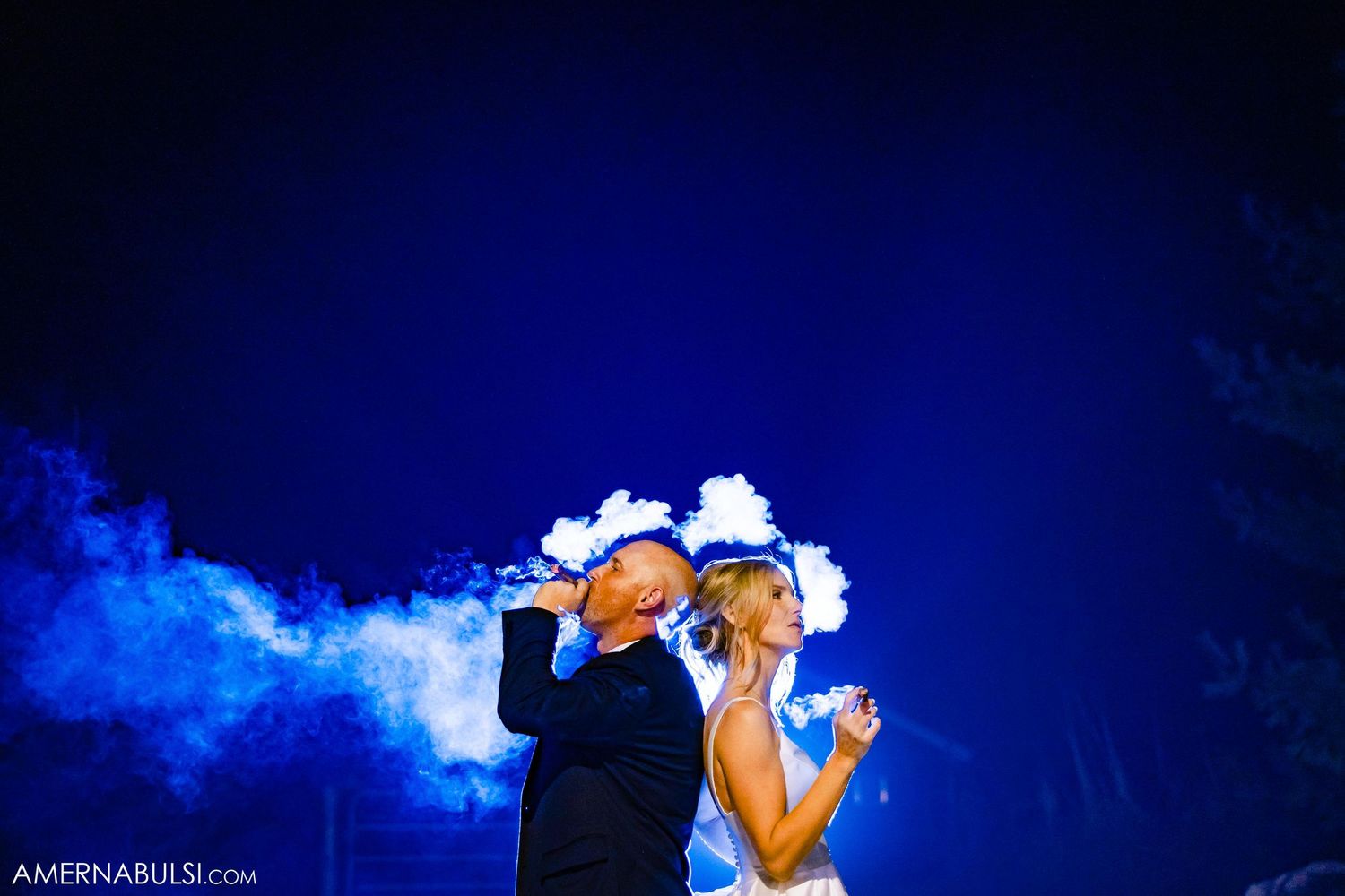 Creative nighttime wedding photo with blue smoke effects against a dark background.