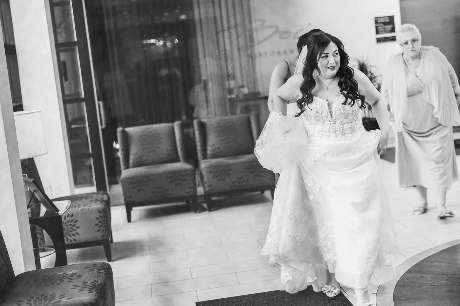 A black and white image of someone in a wedding dress moving through an interior space.