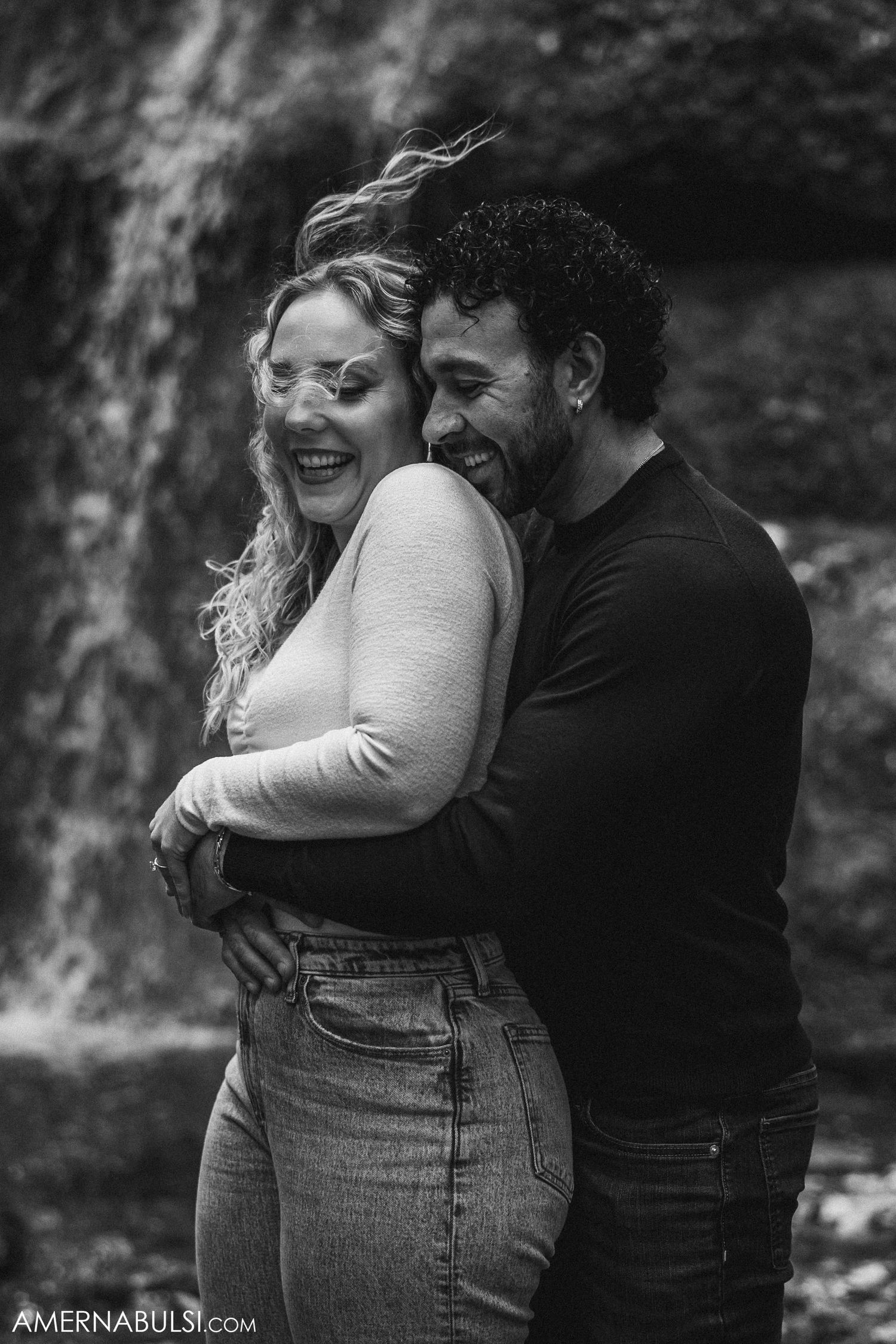 A black and white portrait of a couple sharing a joyful intimate moment by a waterfall.