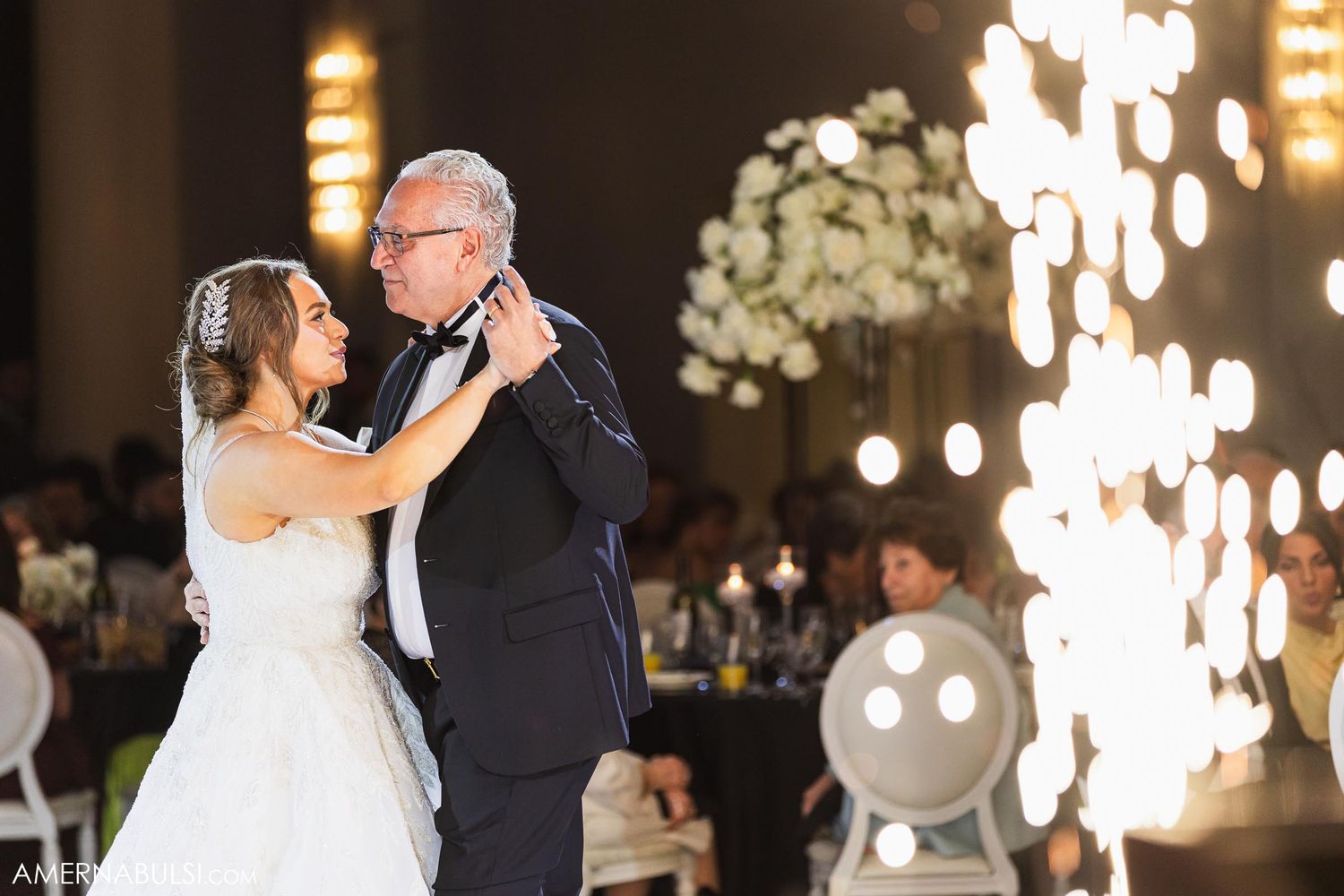 A bride and older man dancing together during a wedding reception with sparklers in the background.