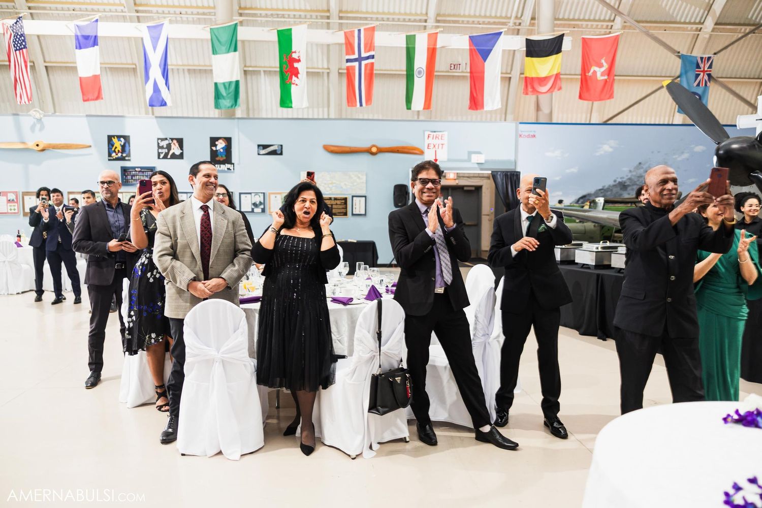 Wedding guests dance and celebrate under international flags at aviation museum reception.