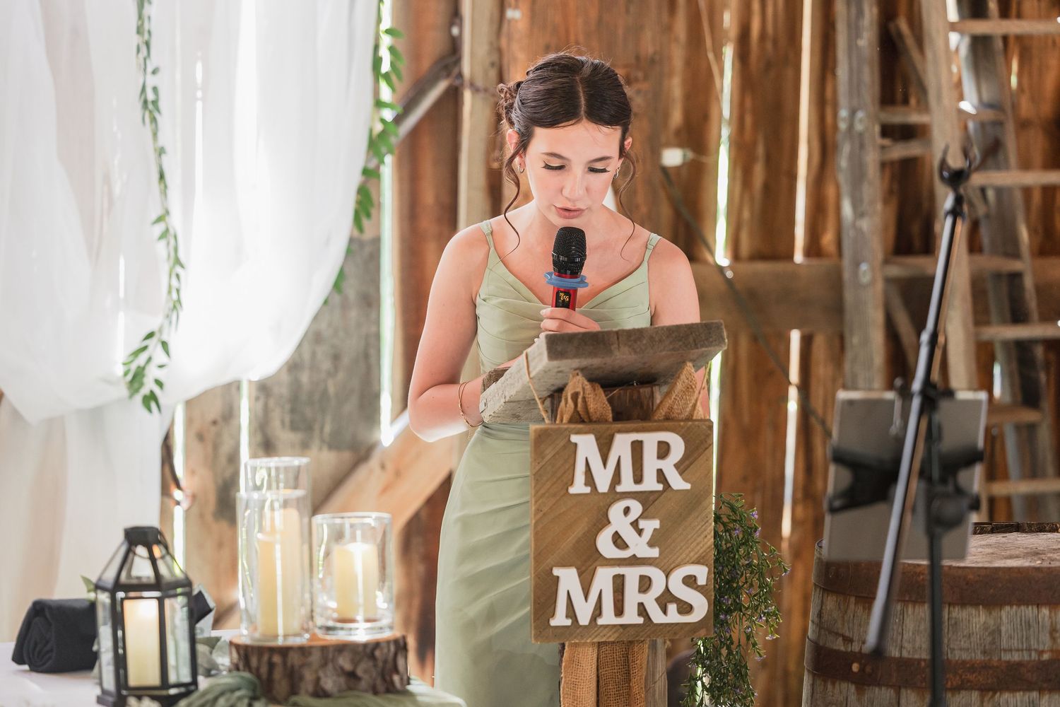 Bridesmaid delivers wedding speech at rustic barn venue podium with Mr & Mrs sign during reception.