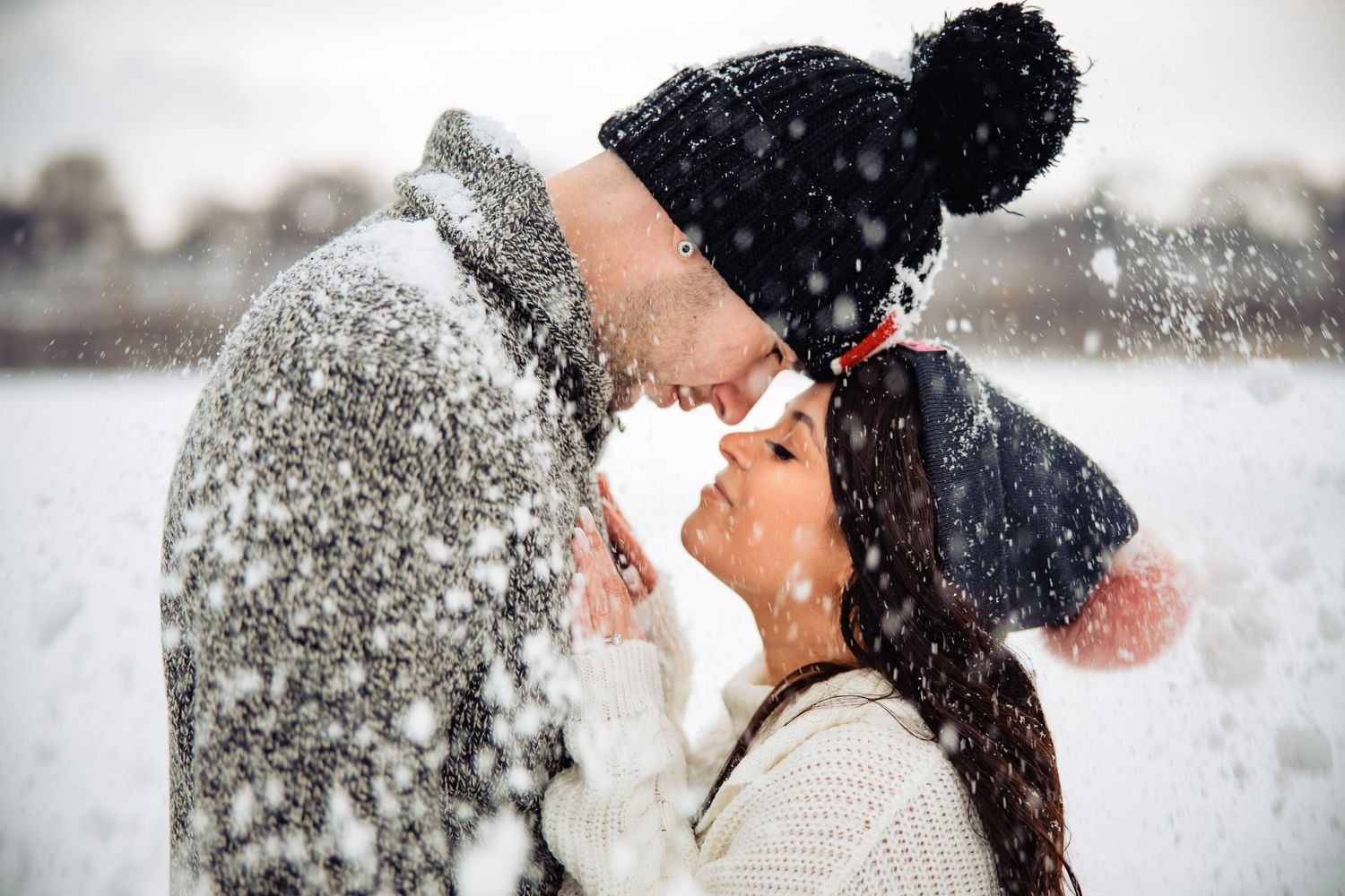 Winter wedding couple embracing in falling snow with dramatic lighting.