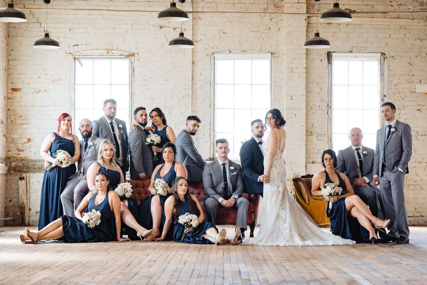 Wedding party gathered in bright industrial loft space with white brick walls and large windows.