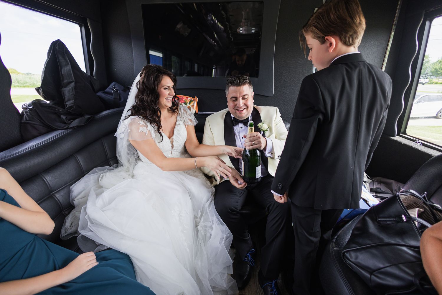Bride and groom celebrate in a limo, toasting champagne with a guest on their wedding day.