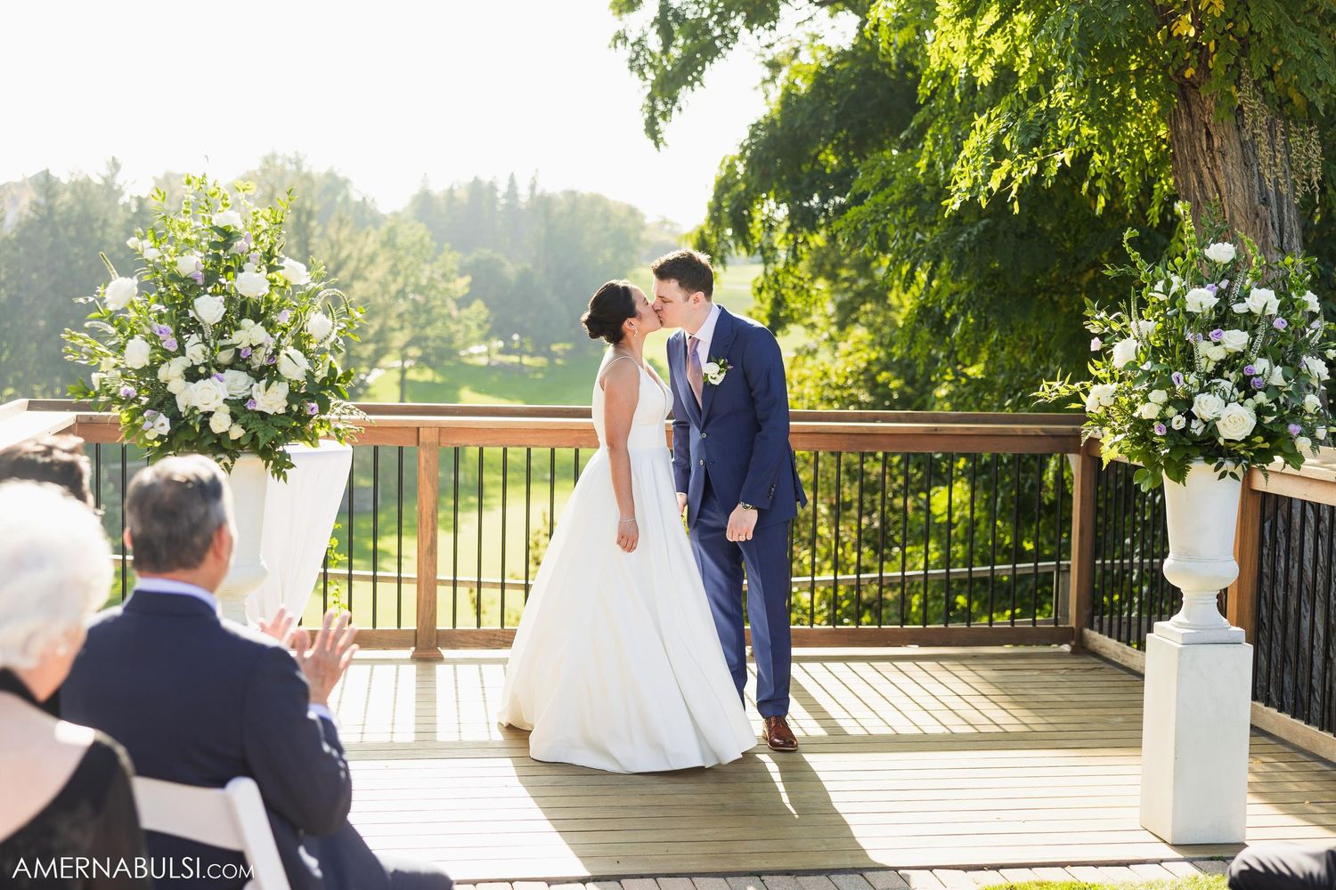 Bride and groom pose for photos on outdoor deck with scenic backdrop.