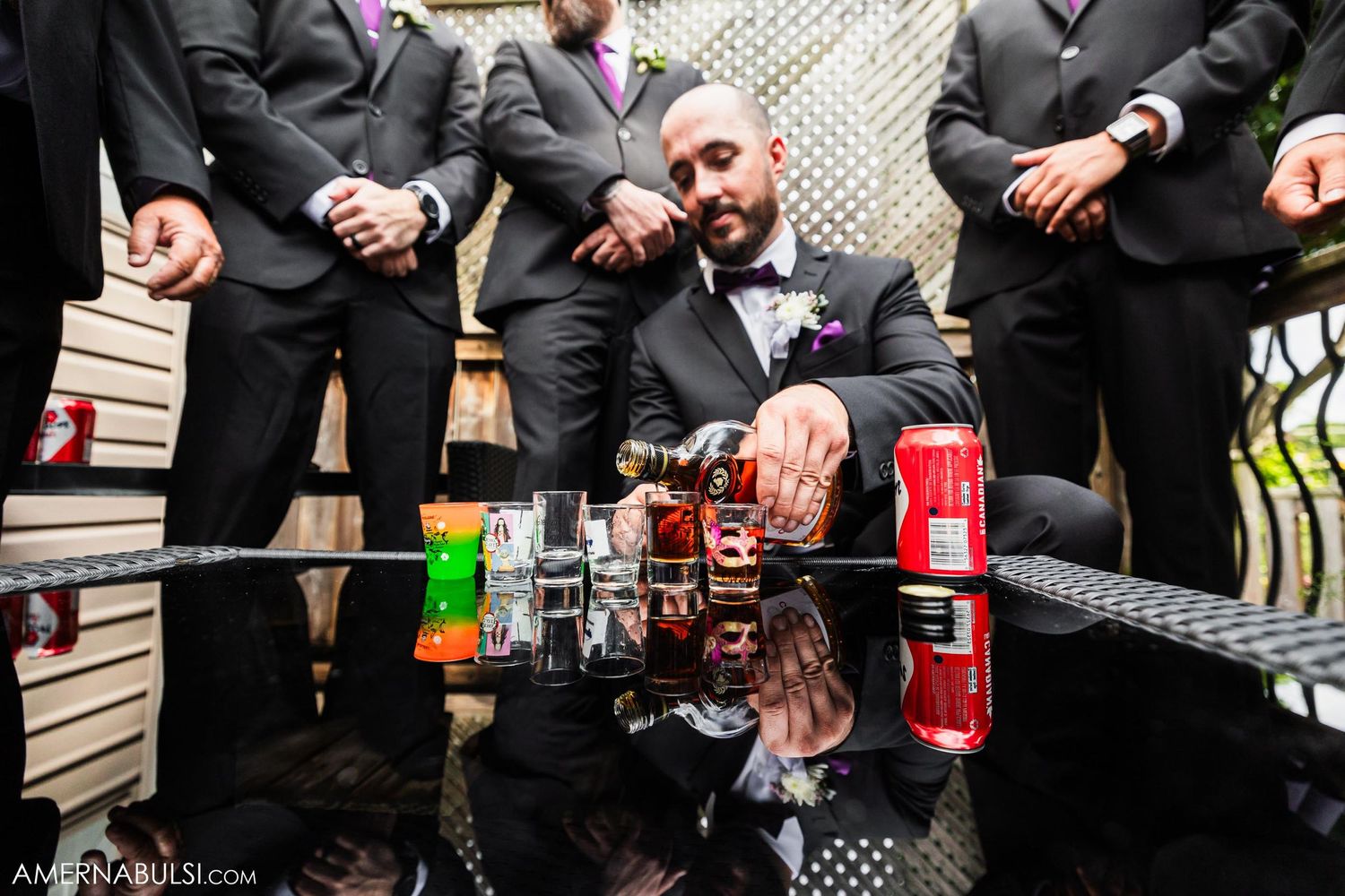 A group in formal attire arranges liquor bottles and drinks on a reflective surface for a celebratory event.