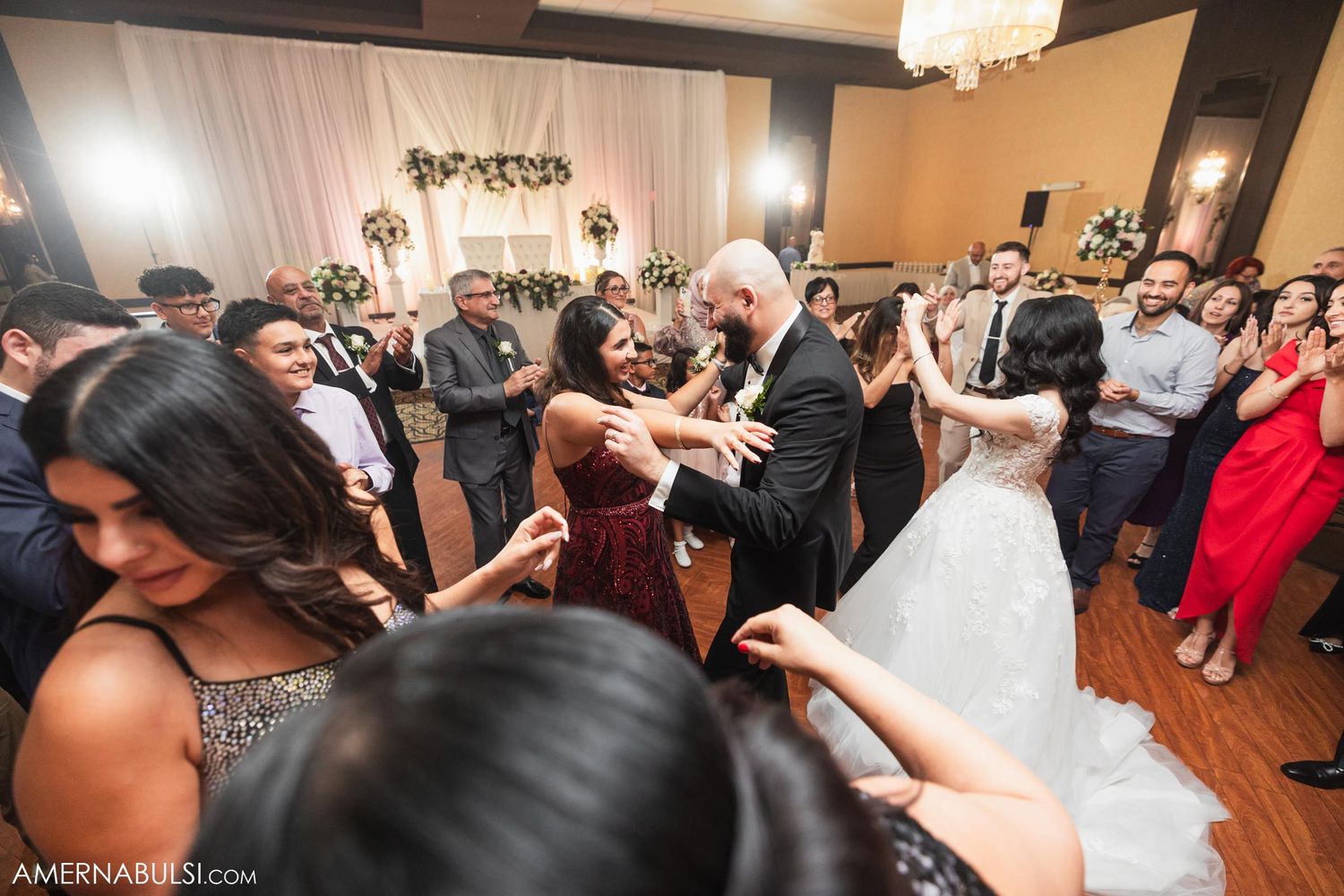 Wedding guests dancing and celebrating with the bride on a crowded dance floor.