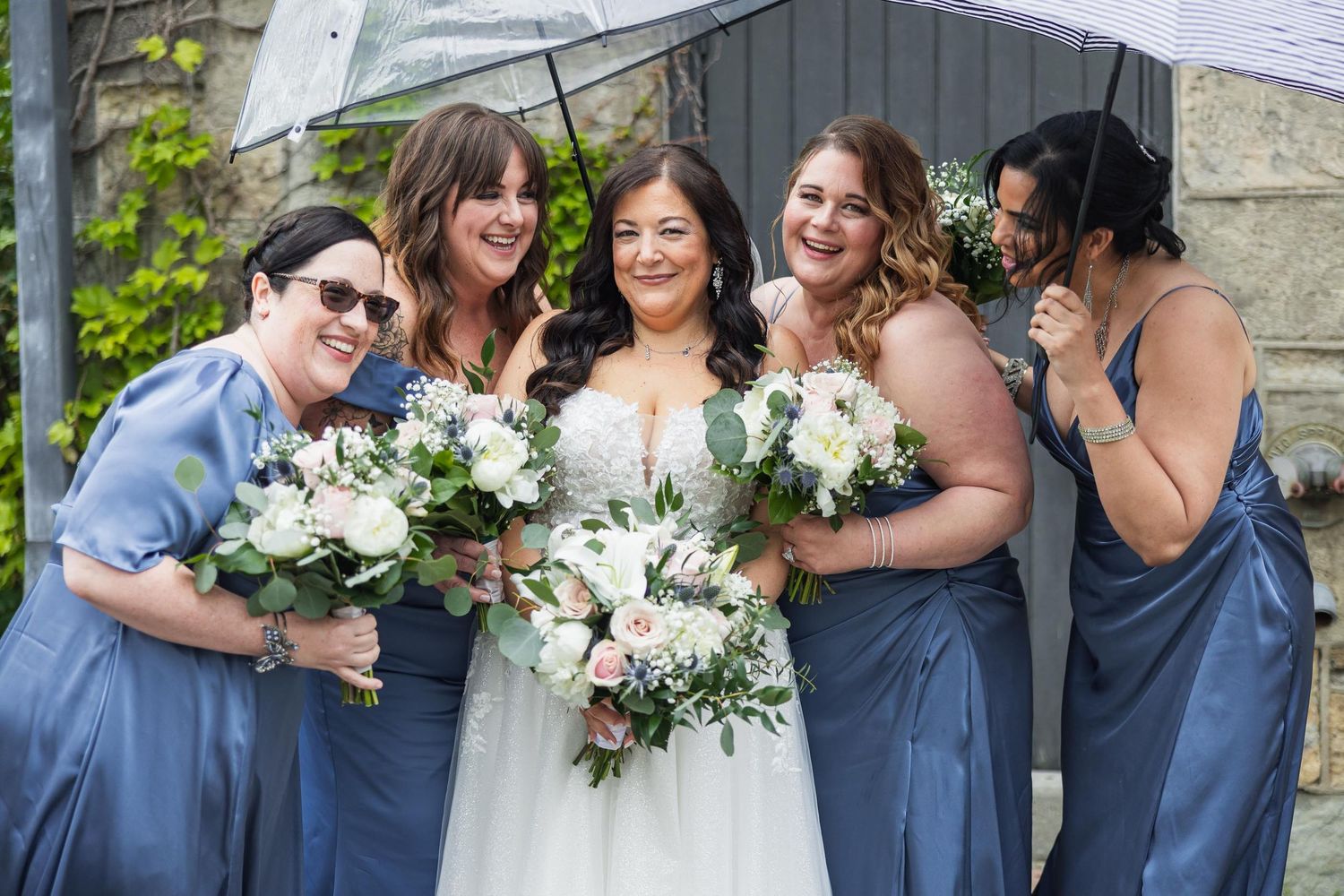 Bridesmaids in blue dresses share joyful moment with white floral bouquets.