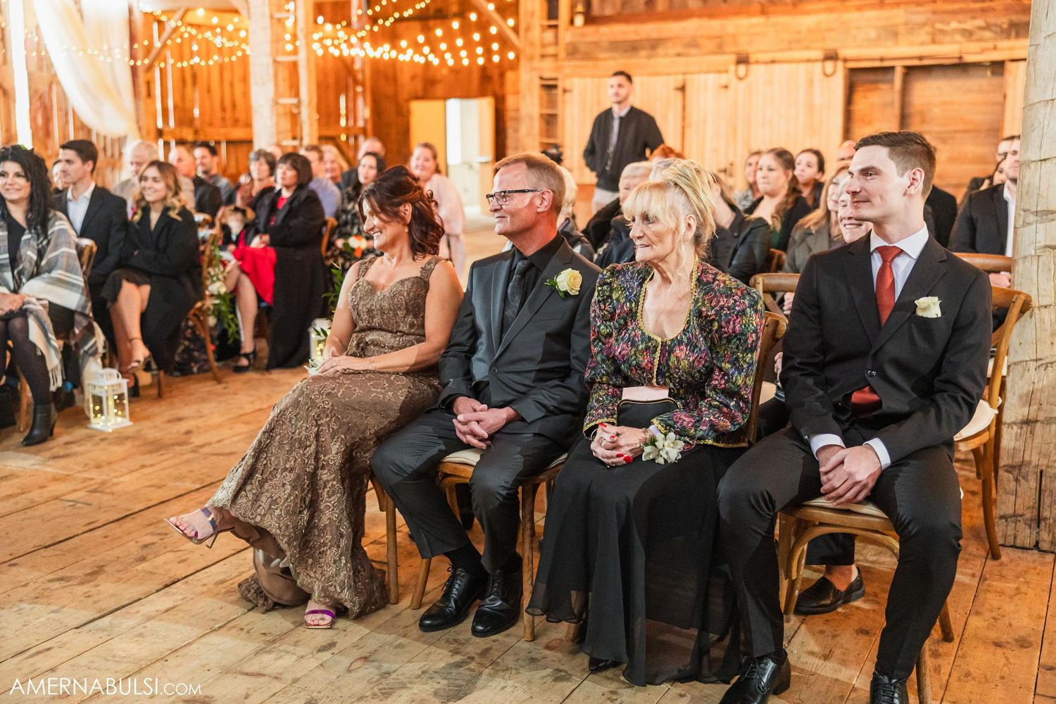 Wedding guests seated on wooden benches inside a beautifully lit rustic barn venue.
