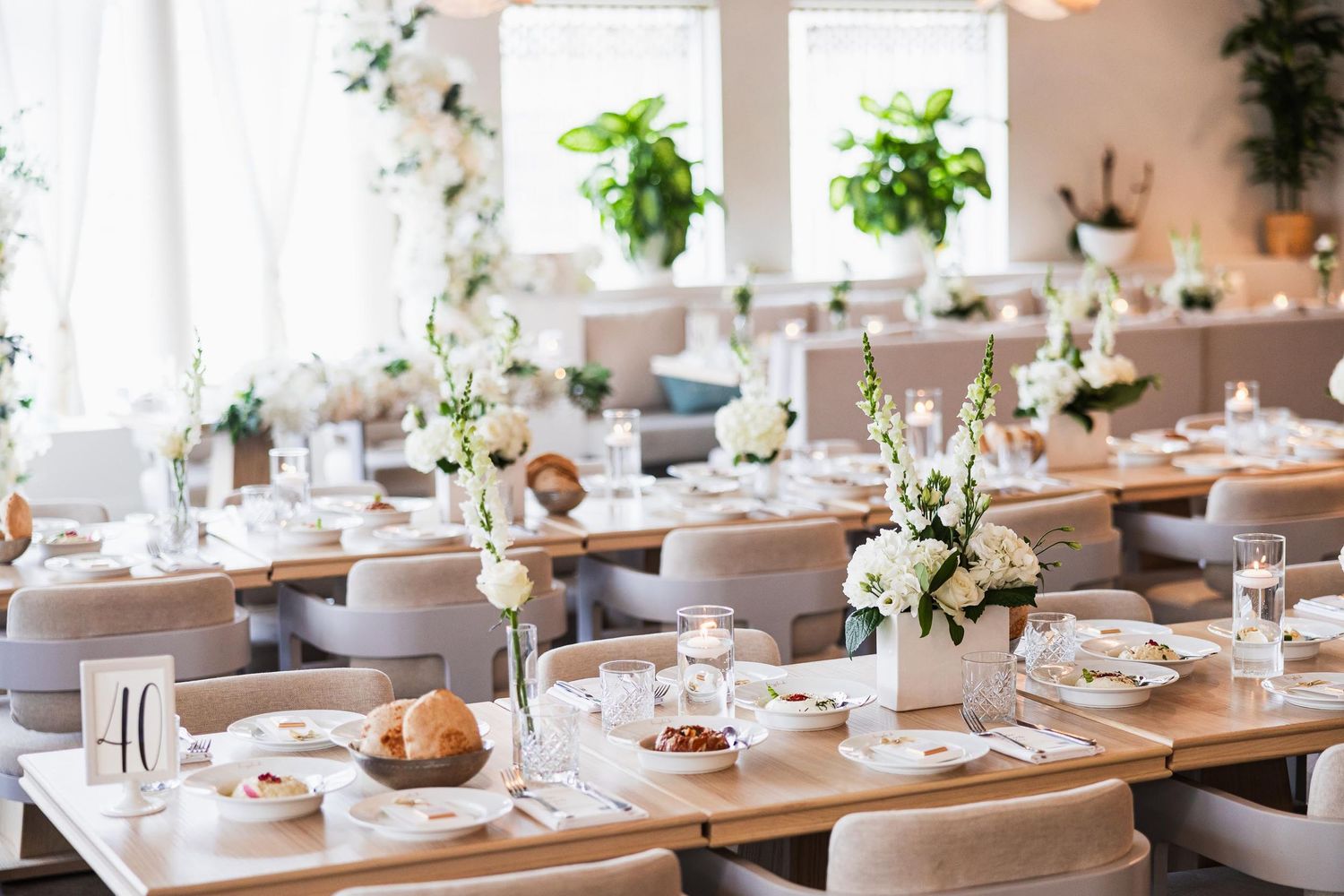 Light-filled reception venue with wooden tables and white floral centerpieces.