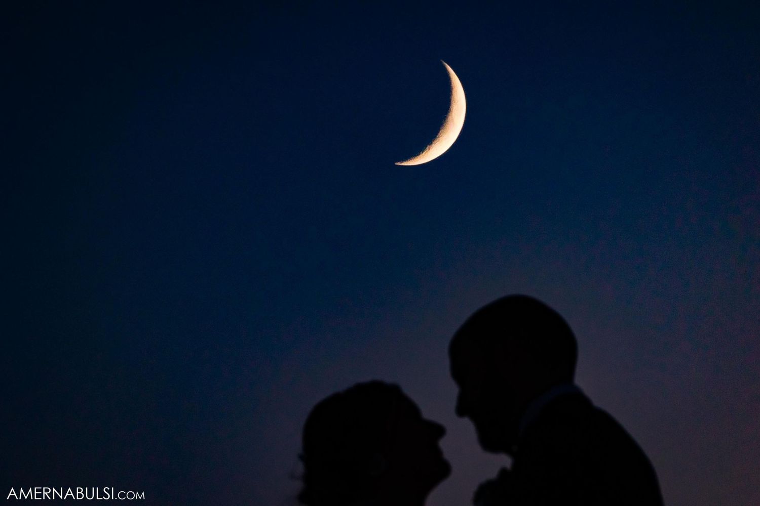 Silhouetted couple against crescent moon in dark night sky.