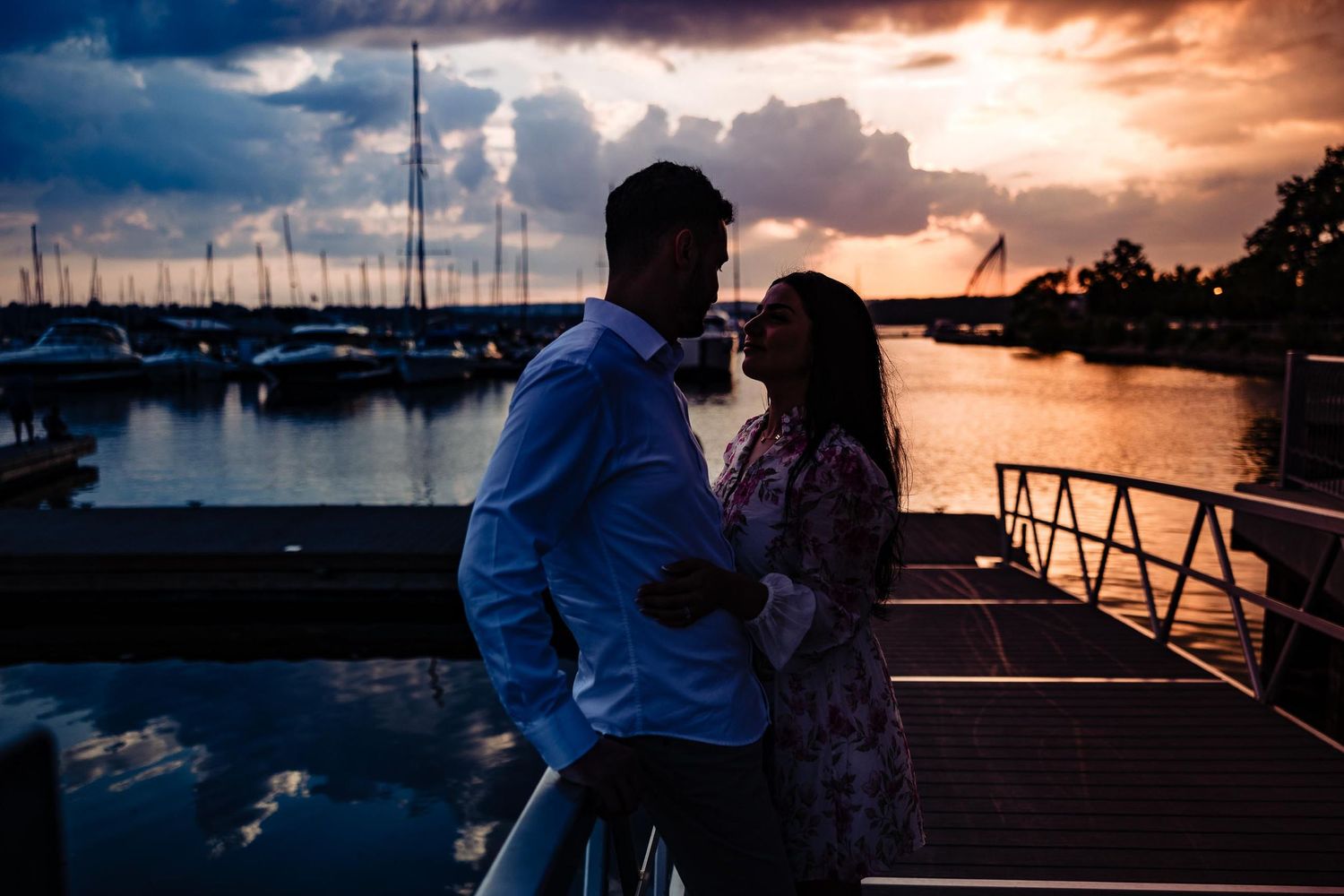 Romantic sunset marina scene with sailboat masts and dramatic sky.